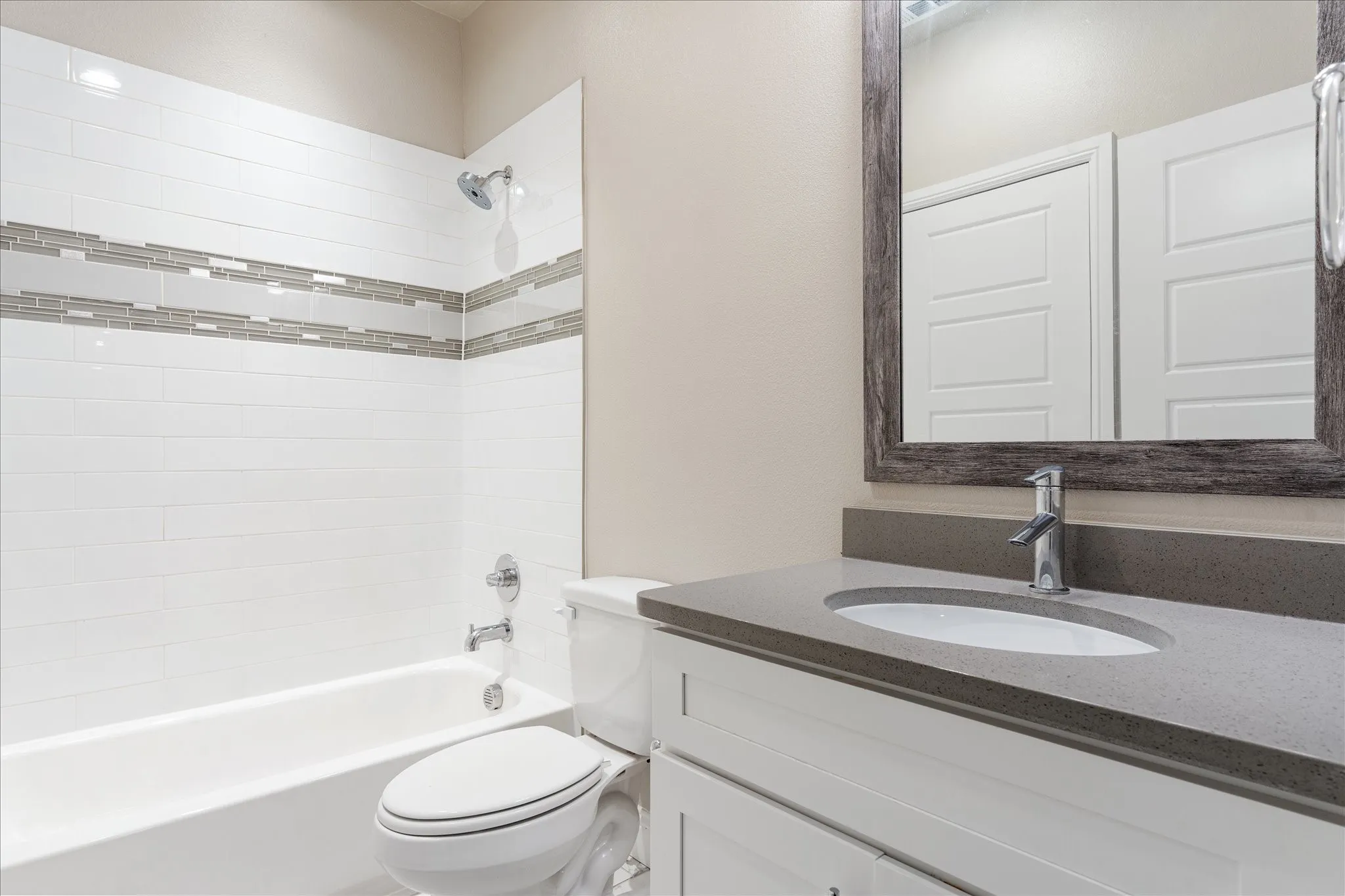Bathroom featuring a white bathtub with subway tile surround, decorative mosaic tile accent, a chrome showerhead, and a white vanity with a gray countertop and chrome faucet