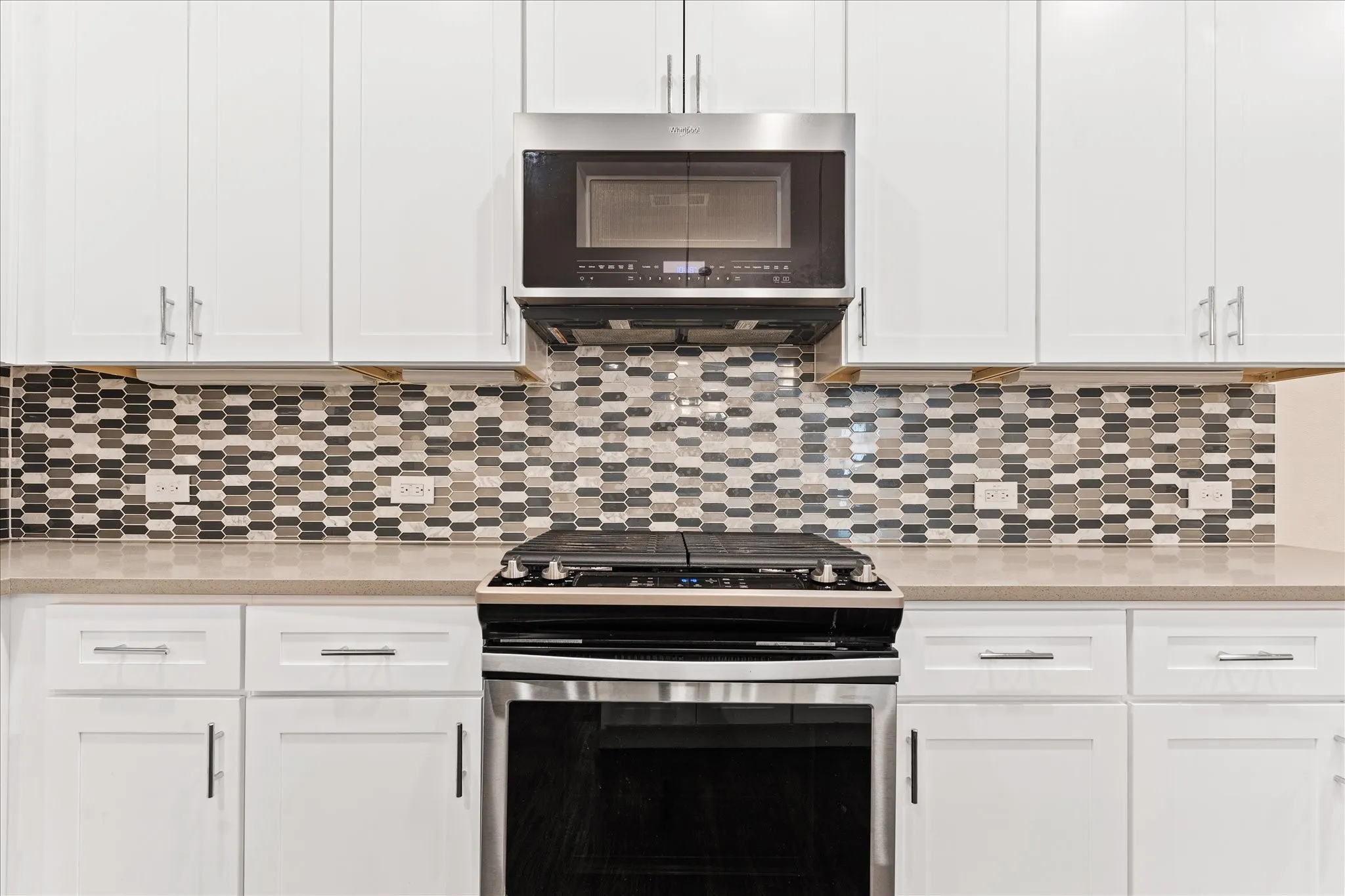 White shaker-style cabinetry, mosaic tile backsplash, light-toned countertop, stainless steel range, and stainless steel microwave