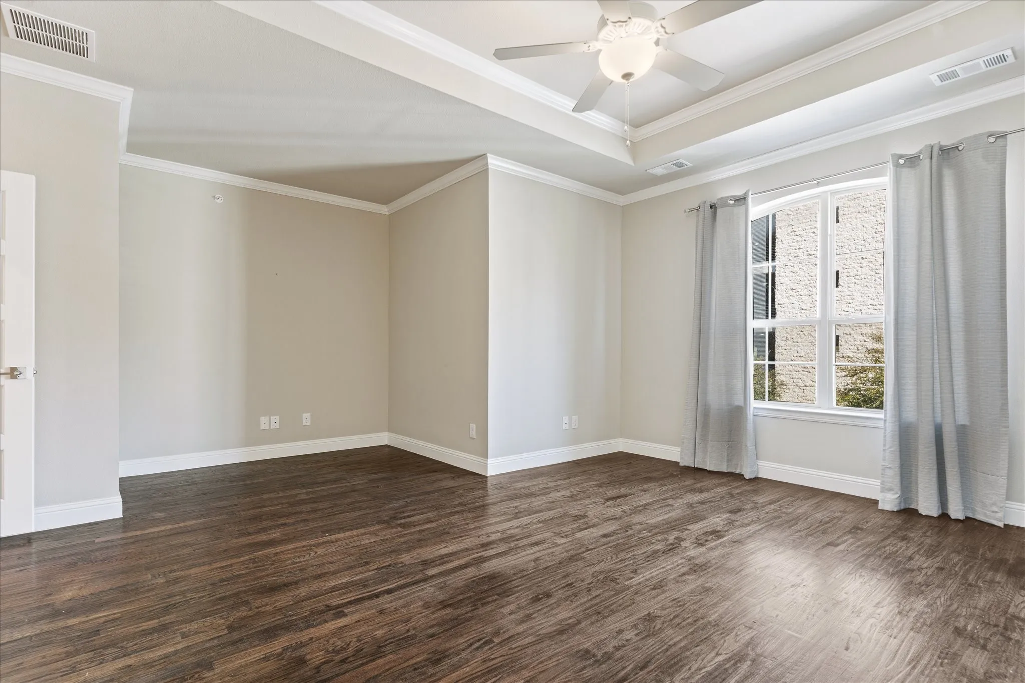 Tray ceiling with a ceiling fan, wood-finish flooring, white trim, and a window with curtains