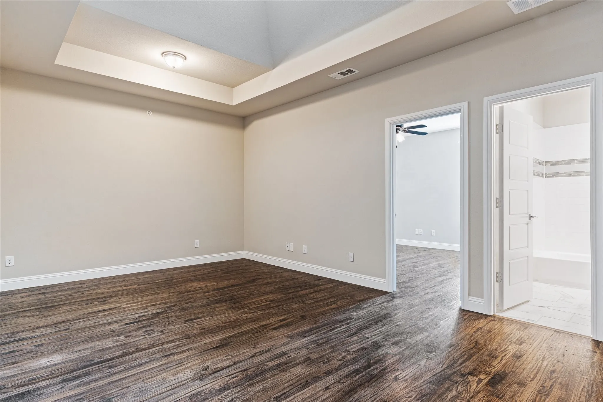 Wood-finish flooring, tray ceiling with flush mount lighting, and neutral wall tones