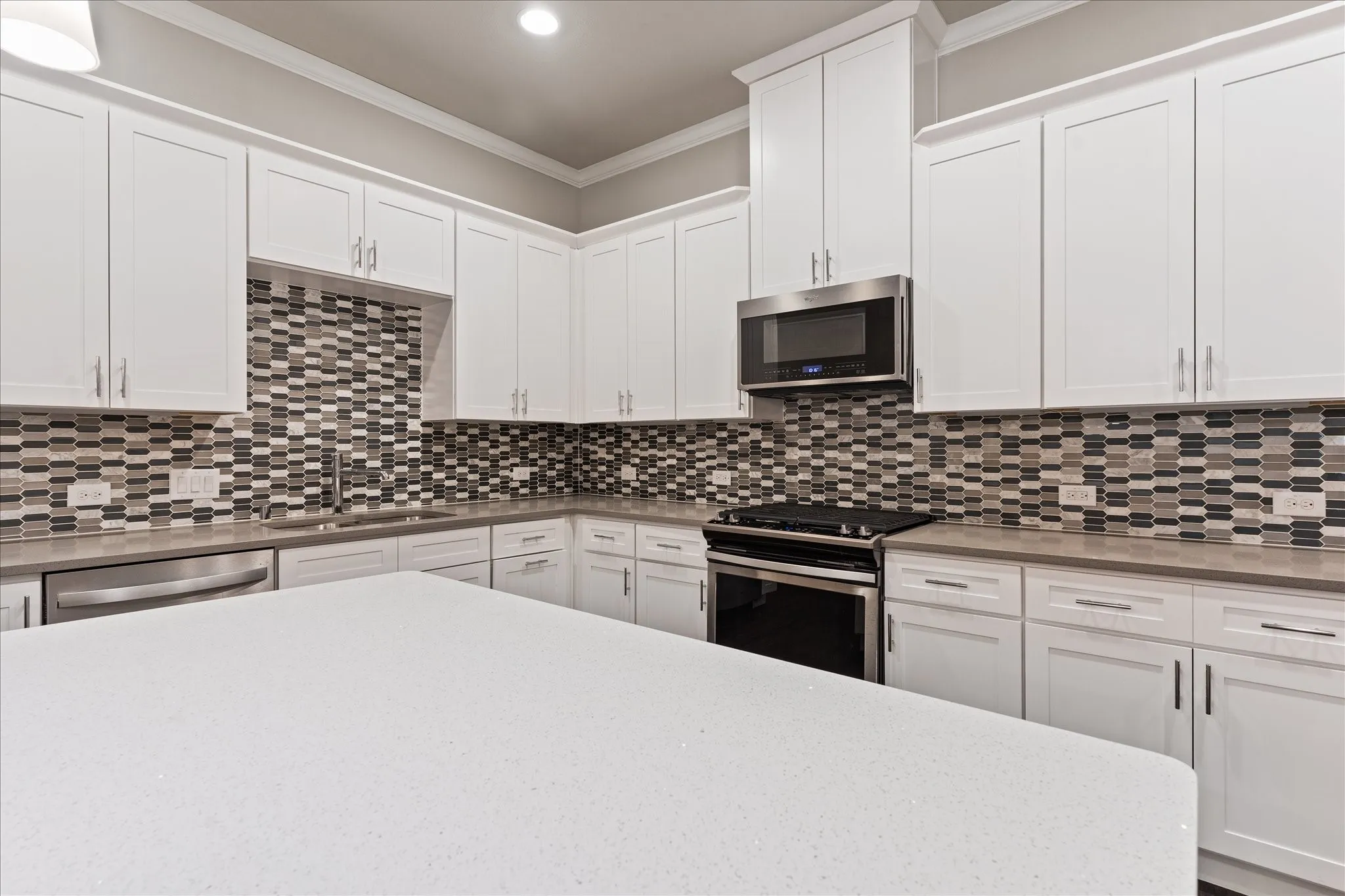 White shaker cabinetry, mosaic tile backsplash, stainless steel appliances, light-toned countertops, and recessed lighting