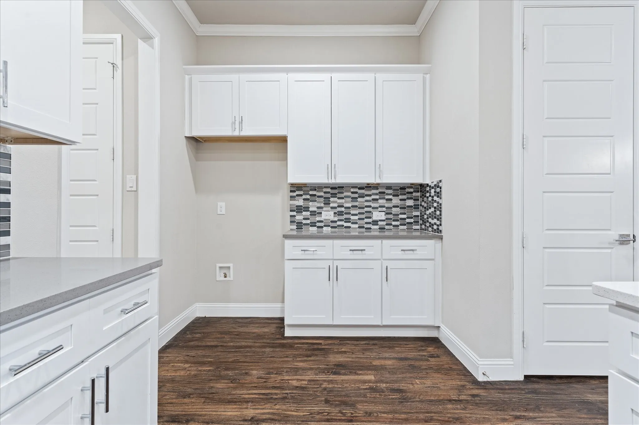 Wood-finish flooring, white shaker-style cabinetry, mosaic tile backsplash, solid surface countertops, and crown molding