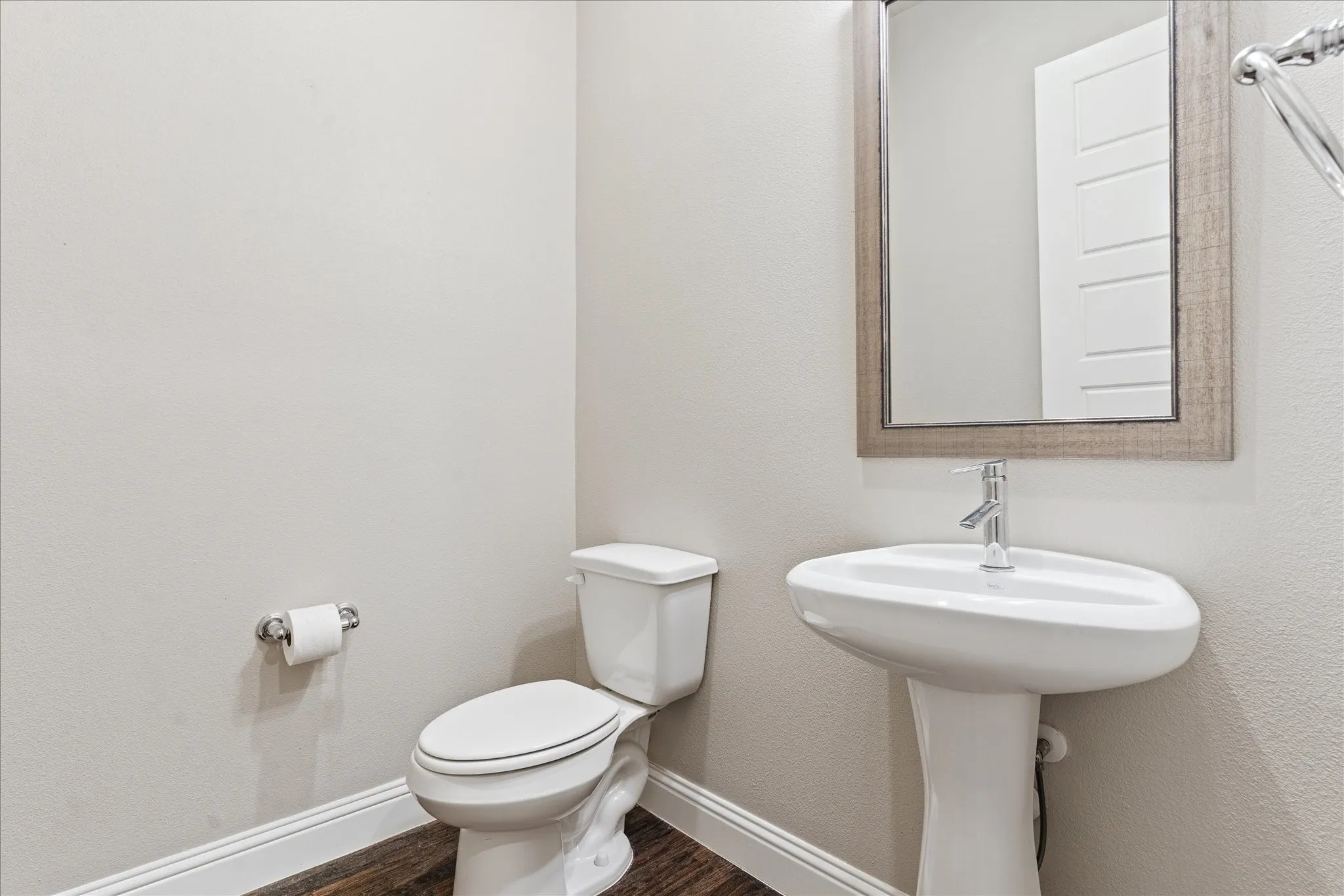 Pedestal sink with chrome faucet, framed mirror, and wood-finish flooring