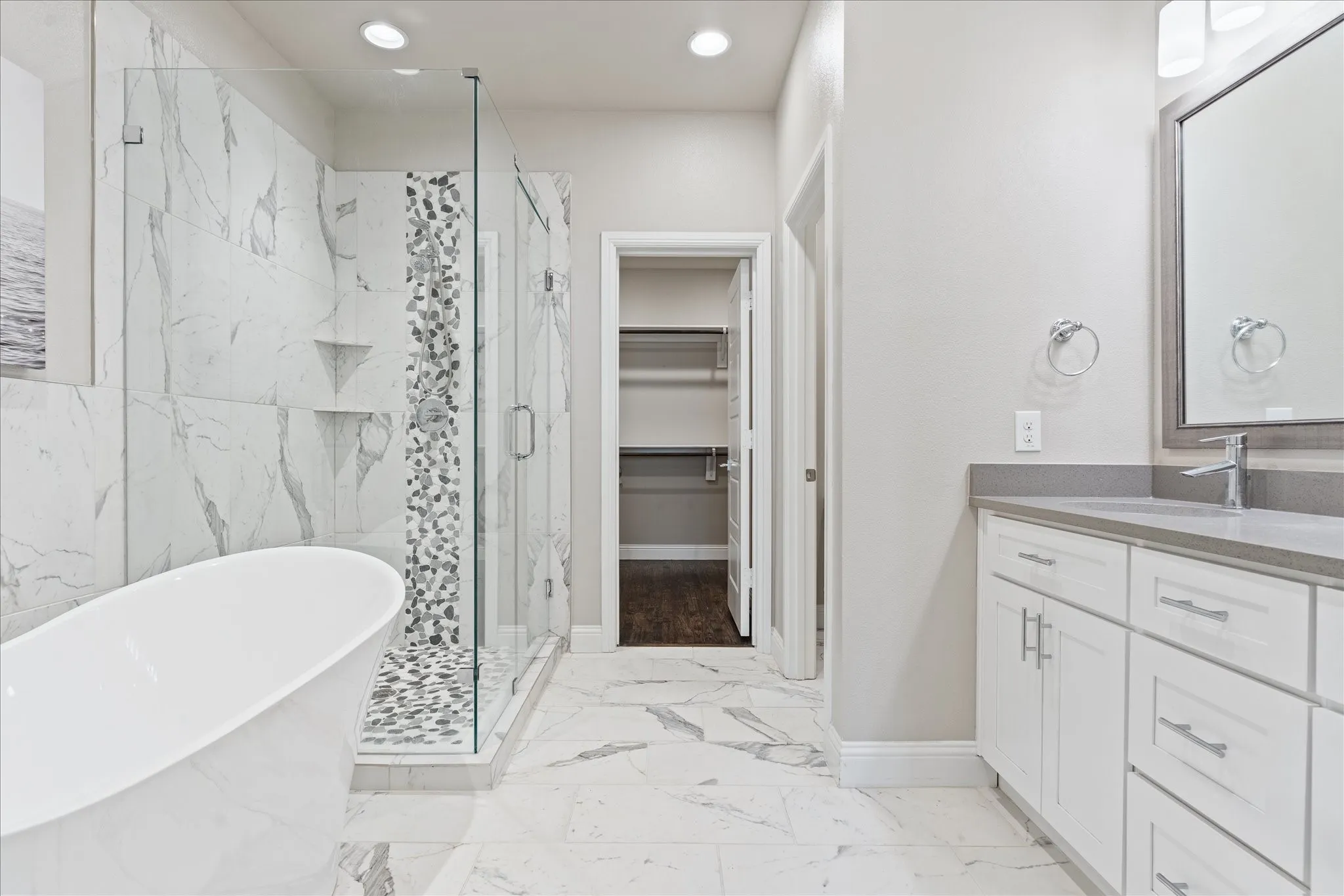 Freestanding soaking tub, walk-in shower with glass enclosure, single vanity with integrated sink, stone countertop, and custom built-in shelving