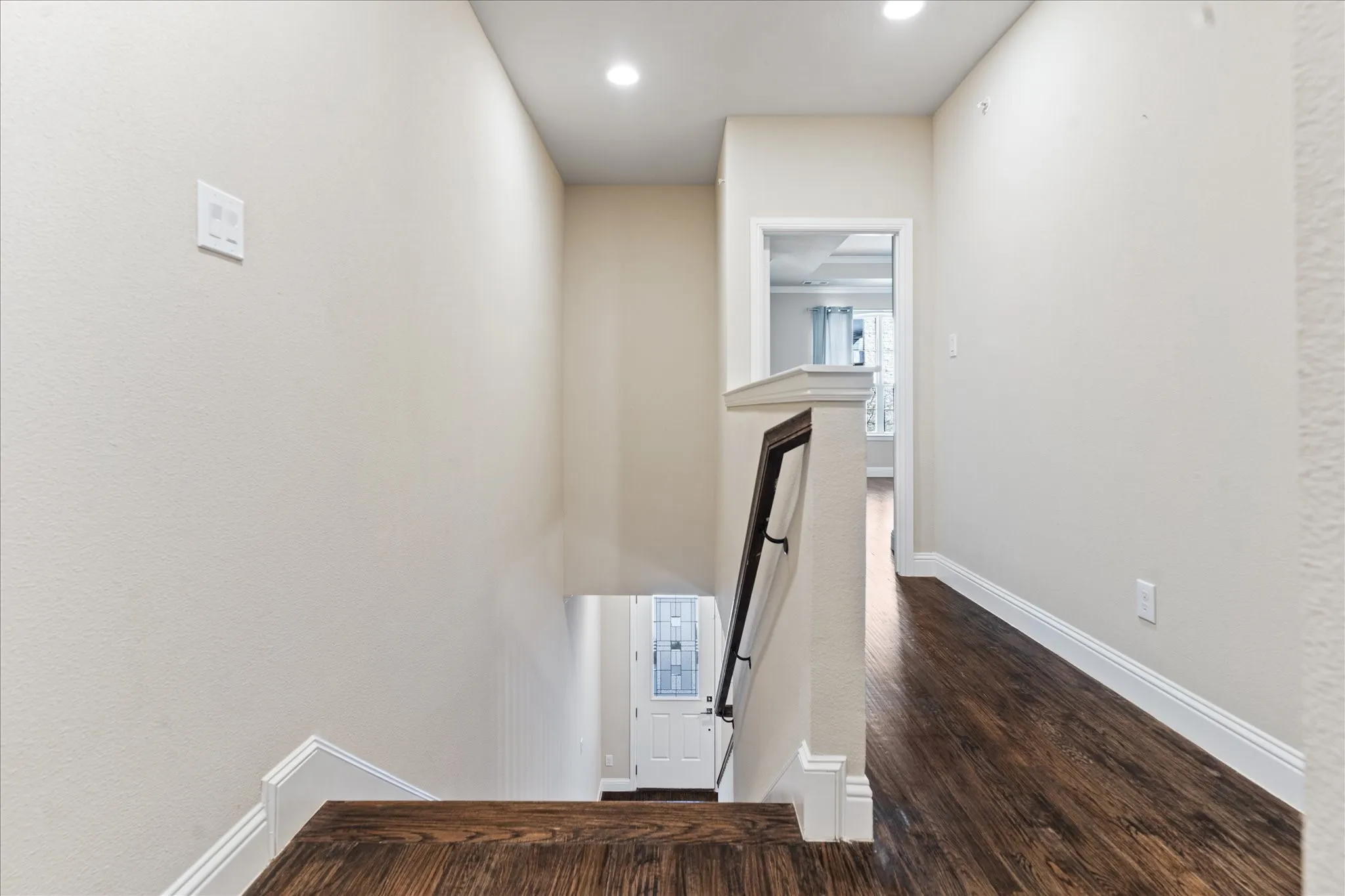 Wood-finish flooring, recessed ceiling lighting, white baseboards, and a dark wood and white stair railing