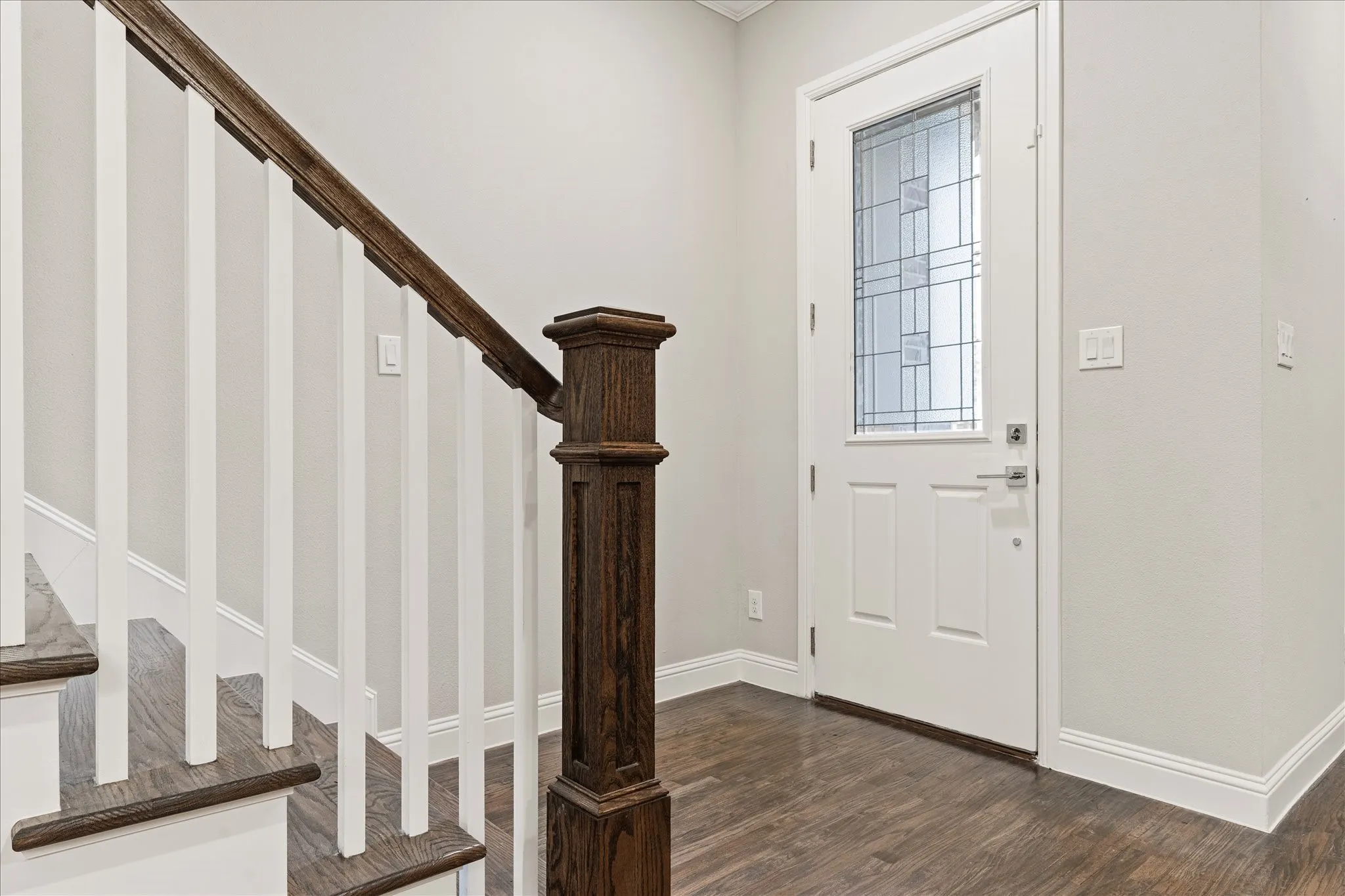 Entryway featuring wood-finish flooring, a white paneled door with leaded glass, white trim, and a staircase with a dark wood-finish handrail and white spindles