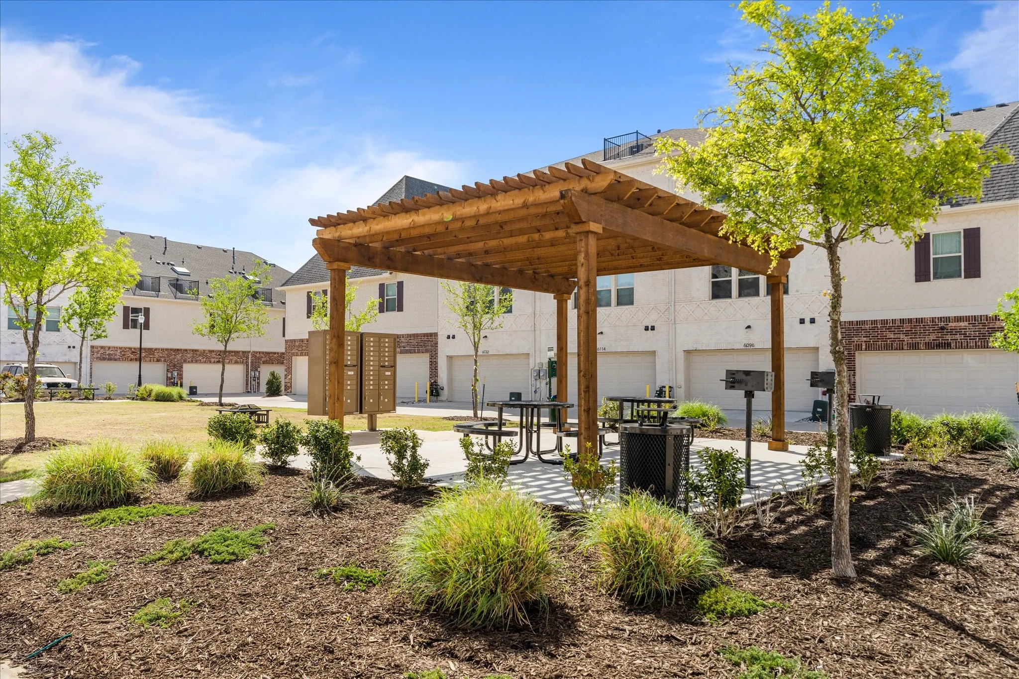 Community green space featuring a wooden pergola, multiple picnic tables, and built-in grilling stations