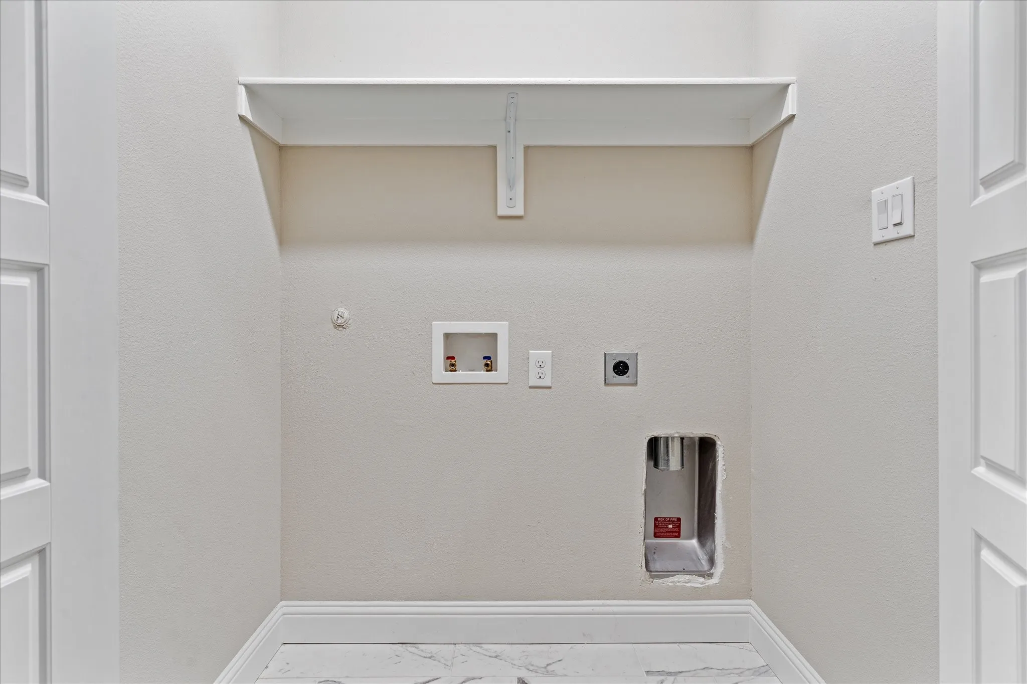 Dedicated laundry alcove featuring a wall-mounted shelf, water hookups, and electrical outlet