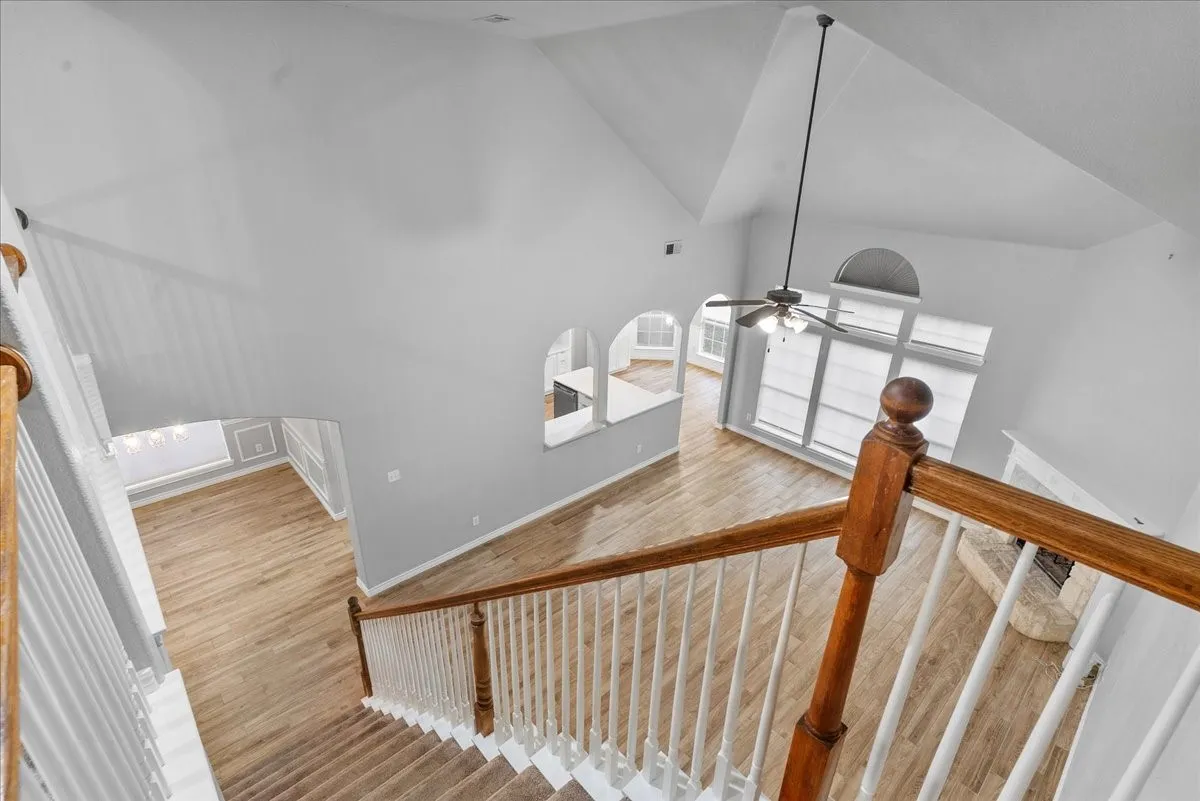 Two-story foyer featuring wood-finish flooring, a traditional wood and white spindle staircase, vaulted ceilings, and arched openings