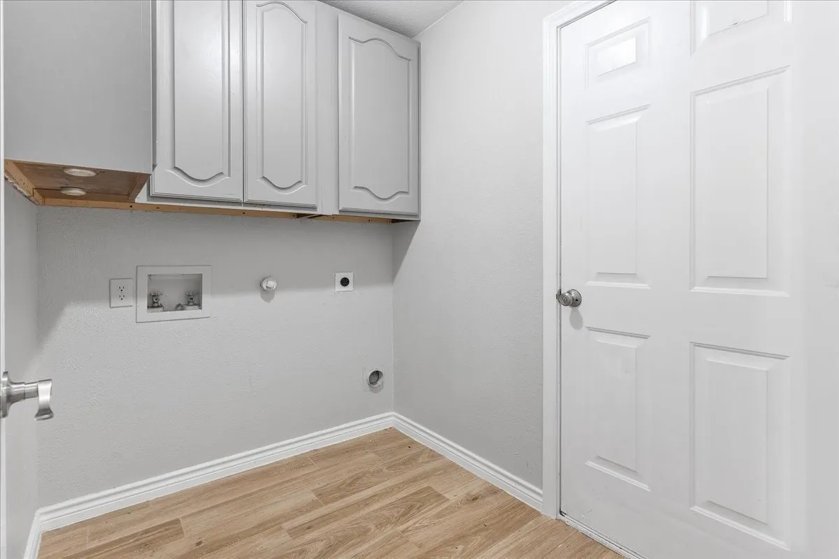 Dedicated utility space featuring light-colored cabinetry, wood-finish flooring, and a panel door
