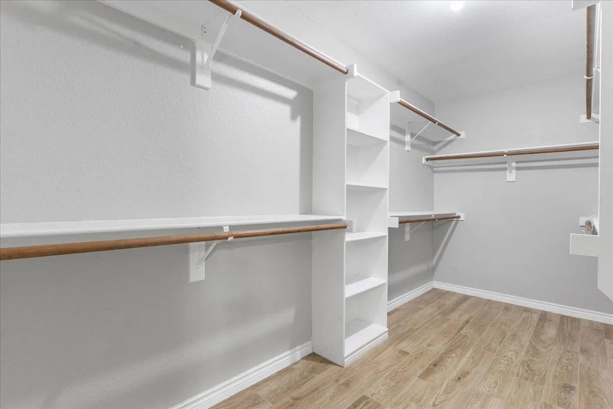 Spacious closet featuring wood-finish flooring, white baseboards, and light gray walls