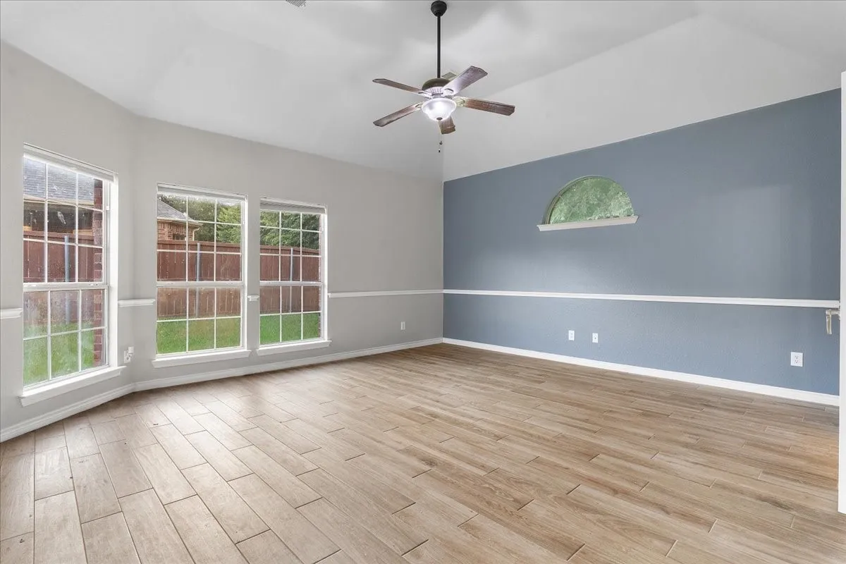 Spacious room featuring wood-finish flooring, vaulted ceilings, and a ceiling fan with integrated lighting