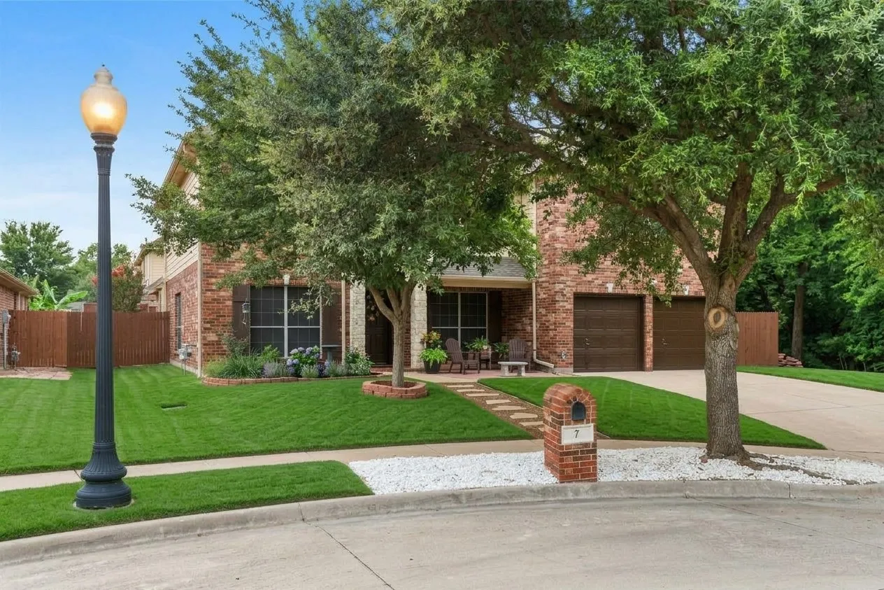 Brick exterior with two-car garage, mature trees, and a concrete driveway