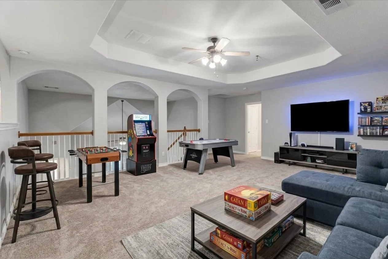 Tray ceiling with a ceiling fan, carpet flooring, archways, and wood handrails
