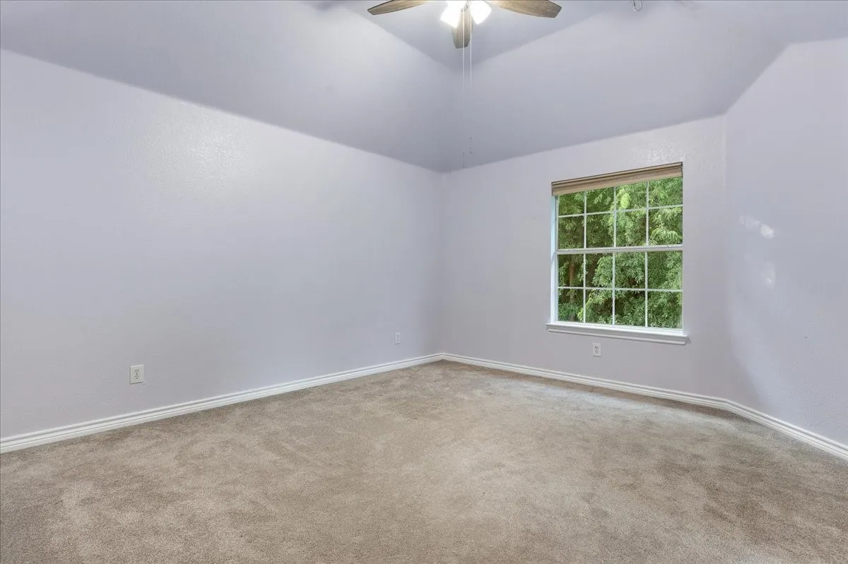 Carpeted room featuring a double-hung window, a ceiling fan, vaulted ceilings, and light-colored walls