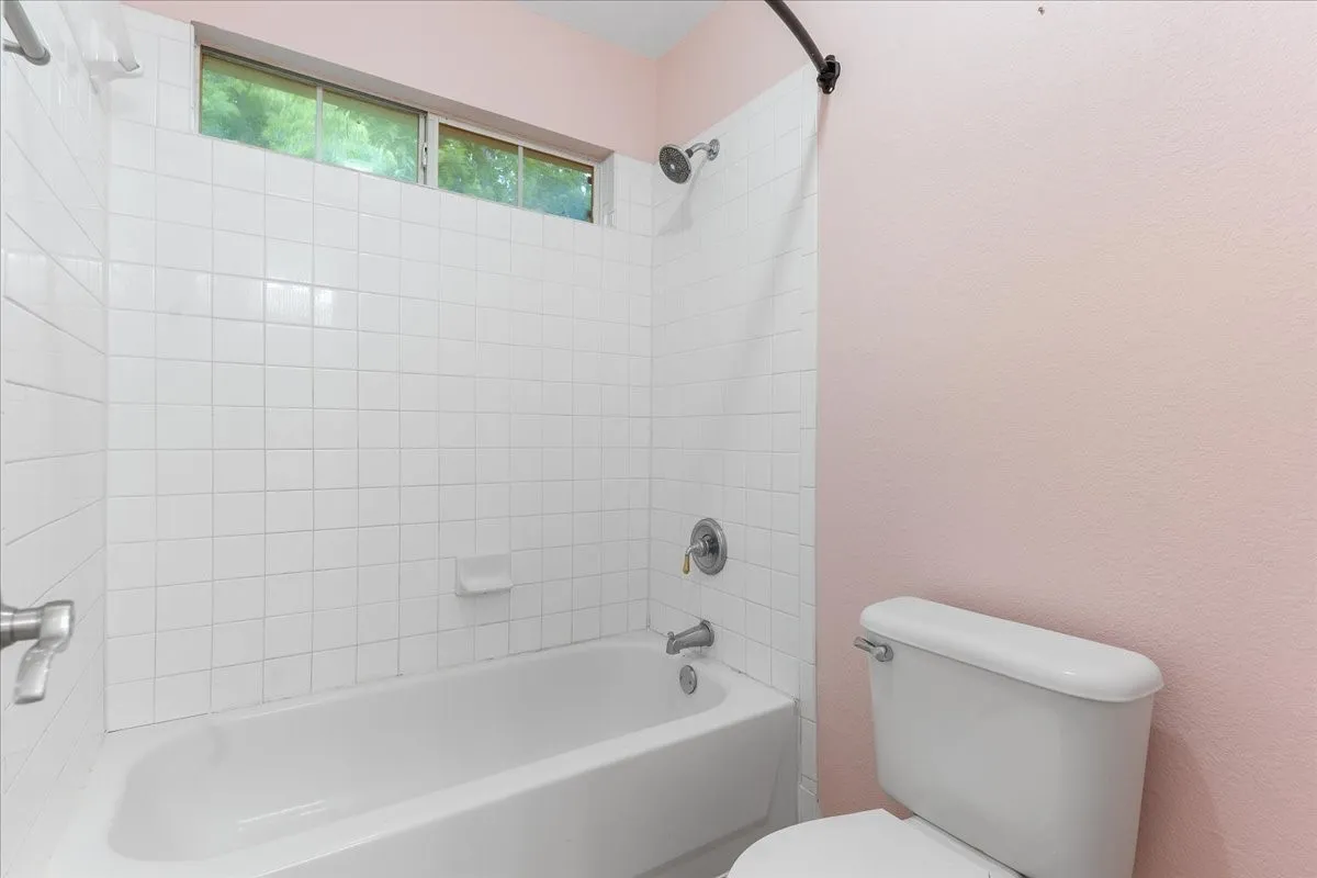 White subway tile bath surround, overhead window, and standard white toilet