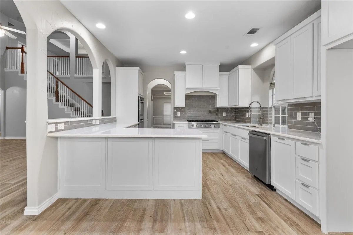 Contemporary kitchen featuring white cabinetry, light-toned wood-finish flooring, stainless steel appliances, a white countertop, and a gray subway tile backsplash