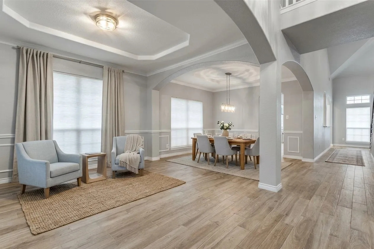 Wood-finish flooring throughout, tray ceiling with recessed lighting, arched doorways, and wainscoting detailing