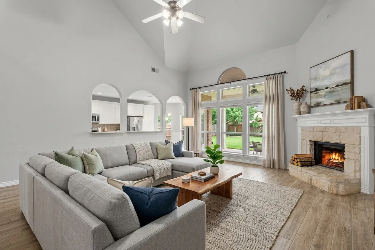 Vaulted ceiling living area with a stone-clad fireplace and mantle, wood-finish flooring, and arched architectural openings