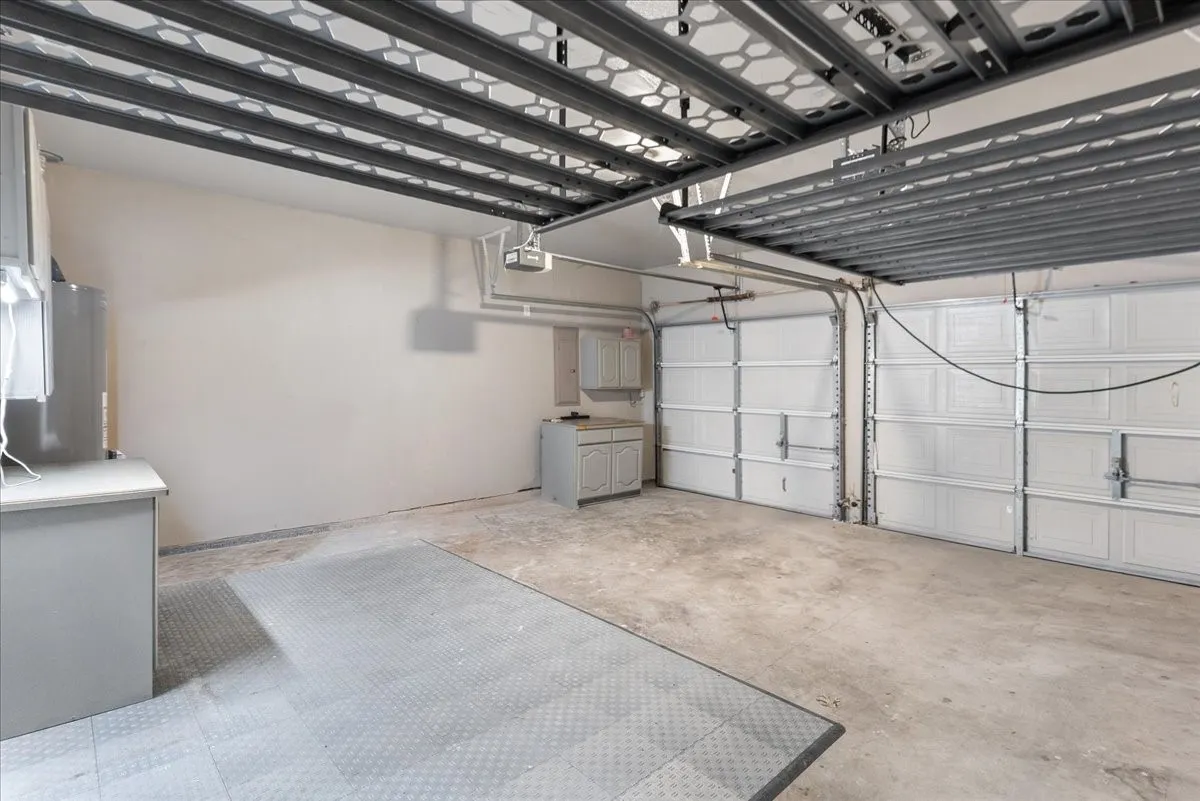 Spacious garage featuring two overhead doors, overhead storage racks, built-in cabinetry, an additional countertop, and a water heater