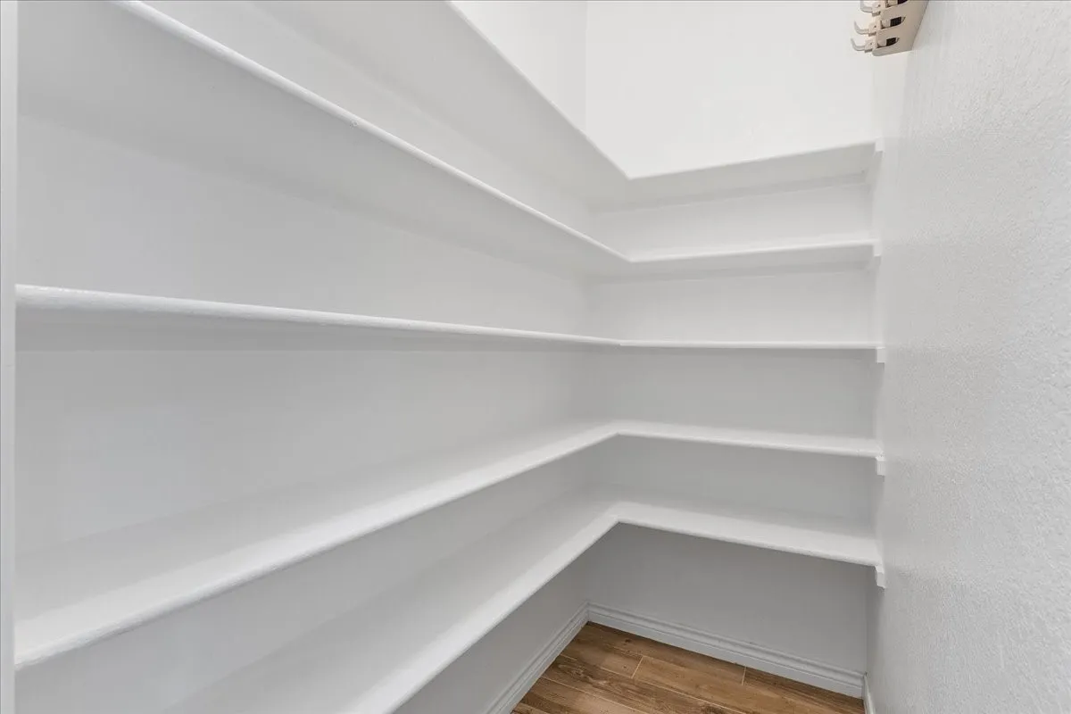 Corner pantry featuring extensive white shelving, textured white walls, white baseboards, and wood-finish flooring