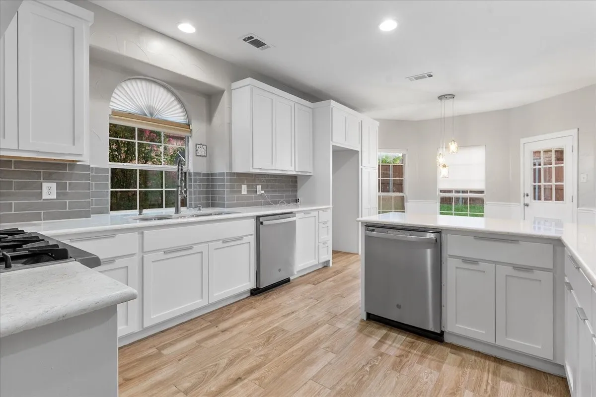 Updated kitchen featuring white shaker cabinetry, stainless steel appliances, wood-finish flooring, a gray subway tile backsplash, and white countertops