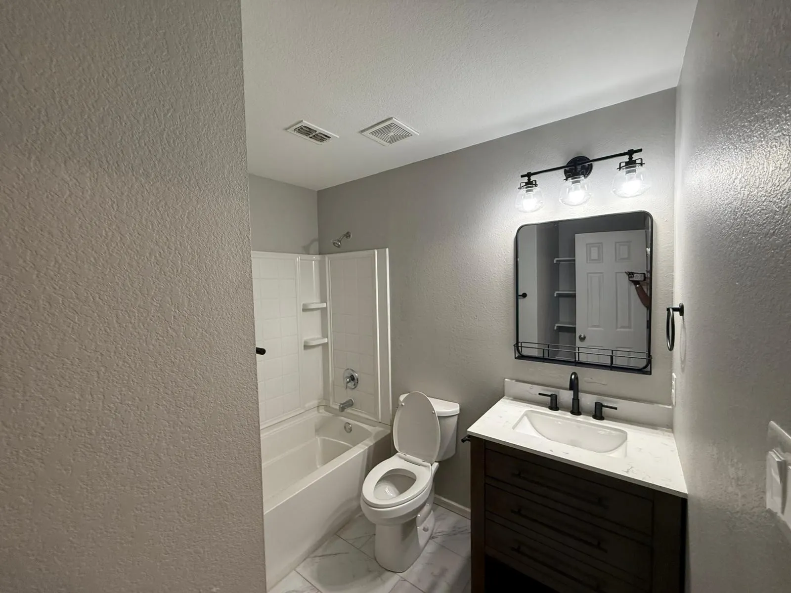 Bathroom featuring a white bathtub, a dark wood-finish vanity, a rectangular vessel sink, and a framed mirror with integrated lighting