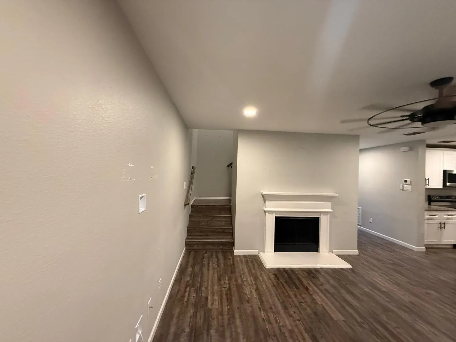 Living area featuring wood-finish flooring, a white mantel fireplace, and a ceiling fan