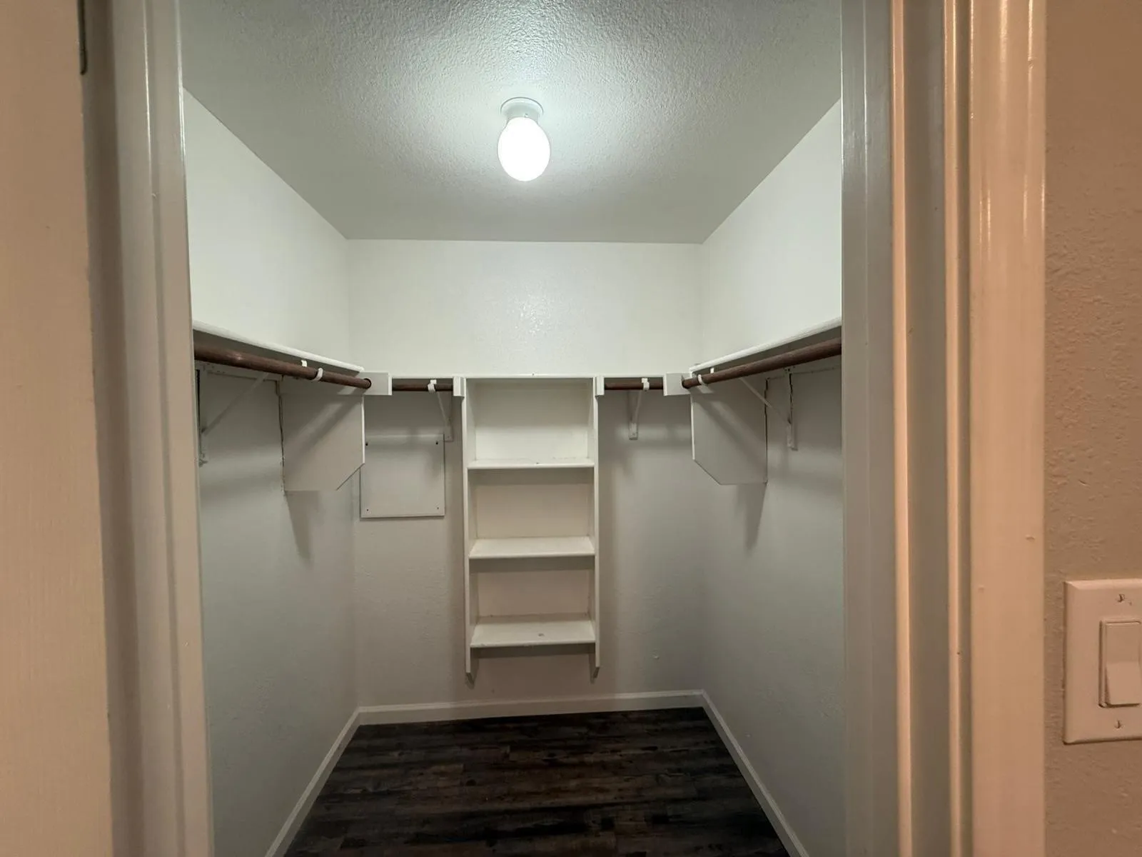 Walk-in closet with integrated shelving, multiple hanging rods, and wood-finish flooring
