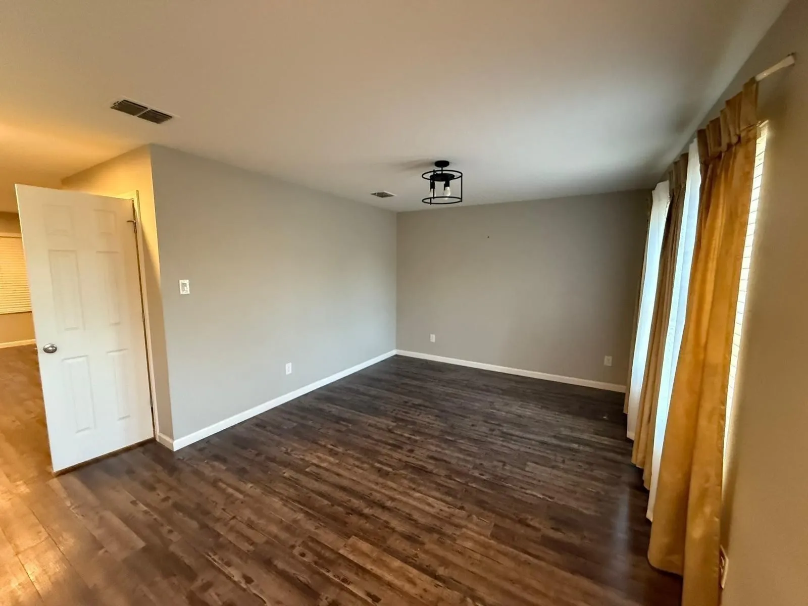 Spacious room featuring wood-finish flooring, neutral wall tones, and a modern ceiling light fixture