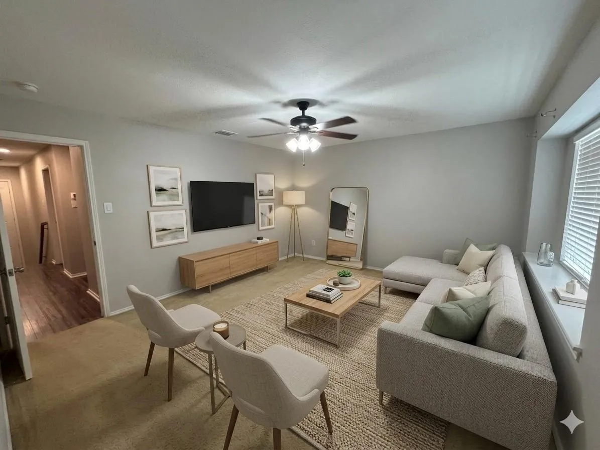 Spacious living area featuring light gray walls, a ceiling fan with integrated lighting, and a large window with blinds