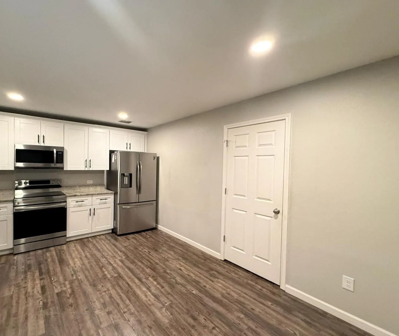 Modern kitchen featuring white shaker-style cabinetry, stainless steel appliances, granite countertops, and wood-finish flooring