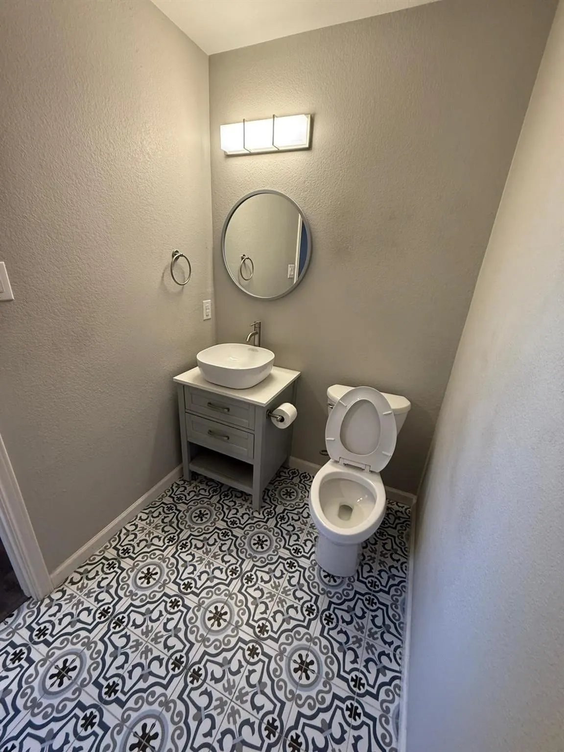 Patterned floor tiling, modern vanity with vessel sink, round wall-mounted mirror, and contemporary light fixture