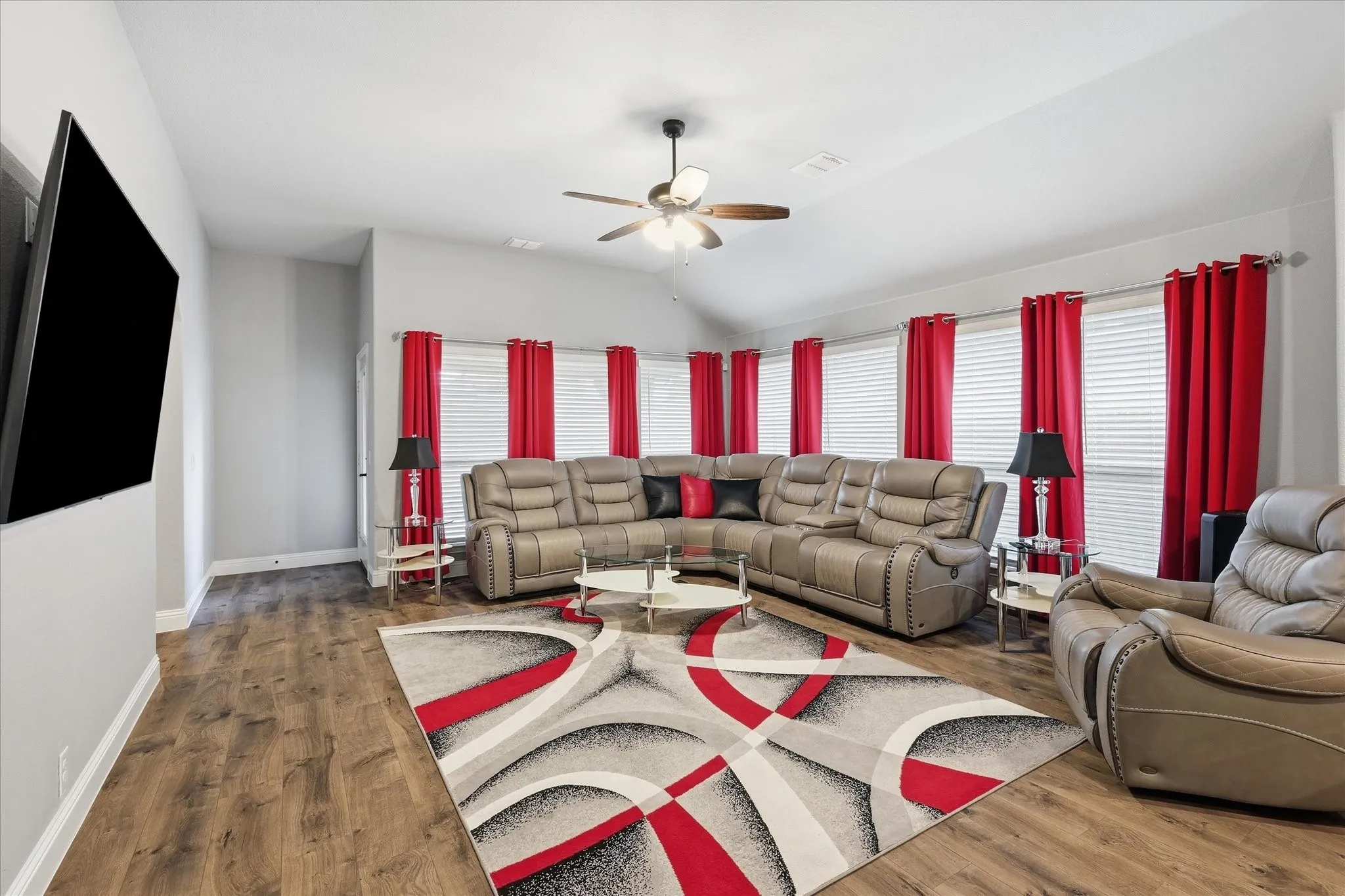 Vaulted ceiling with a ceiling fan, wood-finish flooring, and multiple windows with blinds
