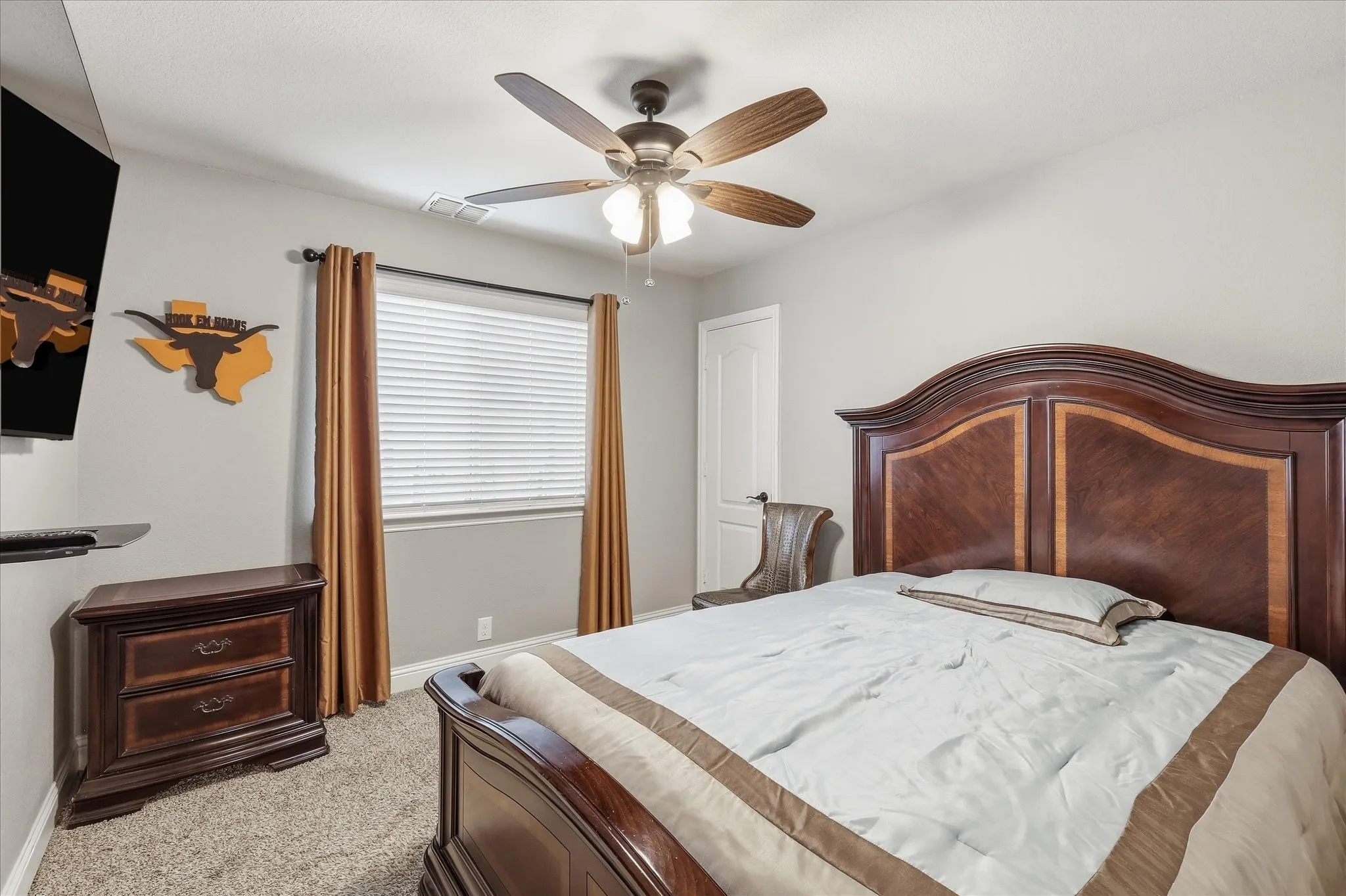 Neutral gray wall paint, textured carpet flooring, window with horizontal blinds, built-in ceiling fan with light, and a white interior door