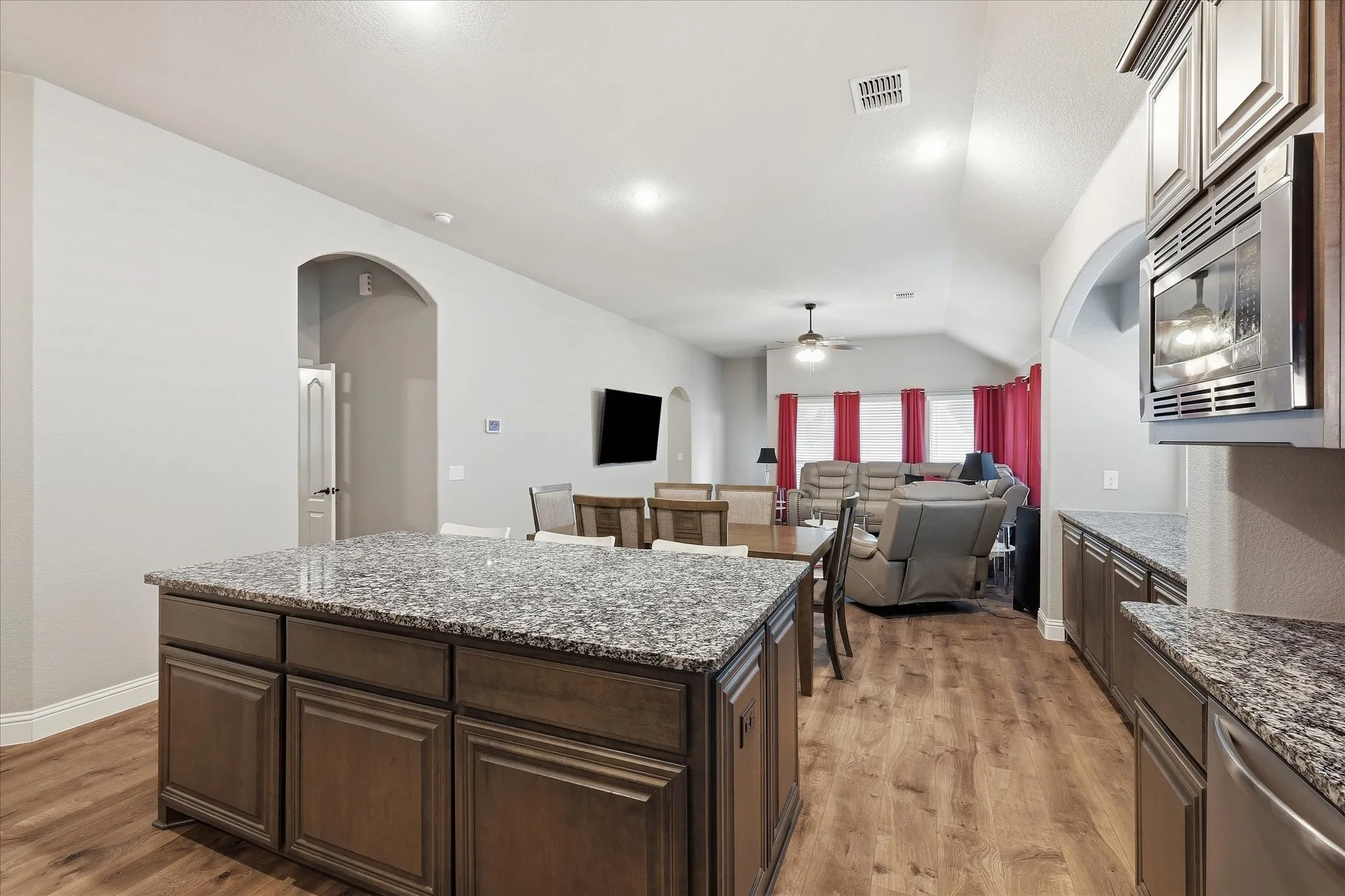 Kitchen island with granite countertop, wood-finish flooring, vaulted ceiling, recessed lighting, and stainless steel built-in microwave