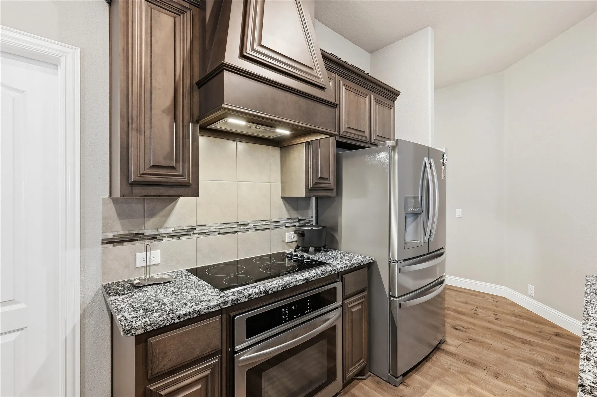 Kitchen featuring wood-finish cabinetry, granite-style countertops, a tile backsplash with mosaic accents, and integrated stainless steel appliances