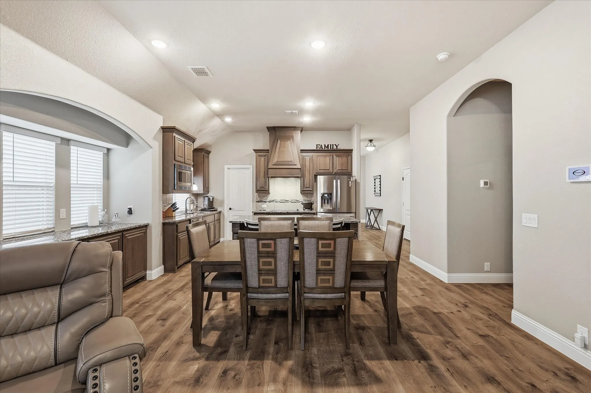 Open-concept living space with wood-finish flooring, recessed lighting, and a kitchen featuring wood cabinetry, stainless steel appliances, and a matching range hood