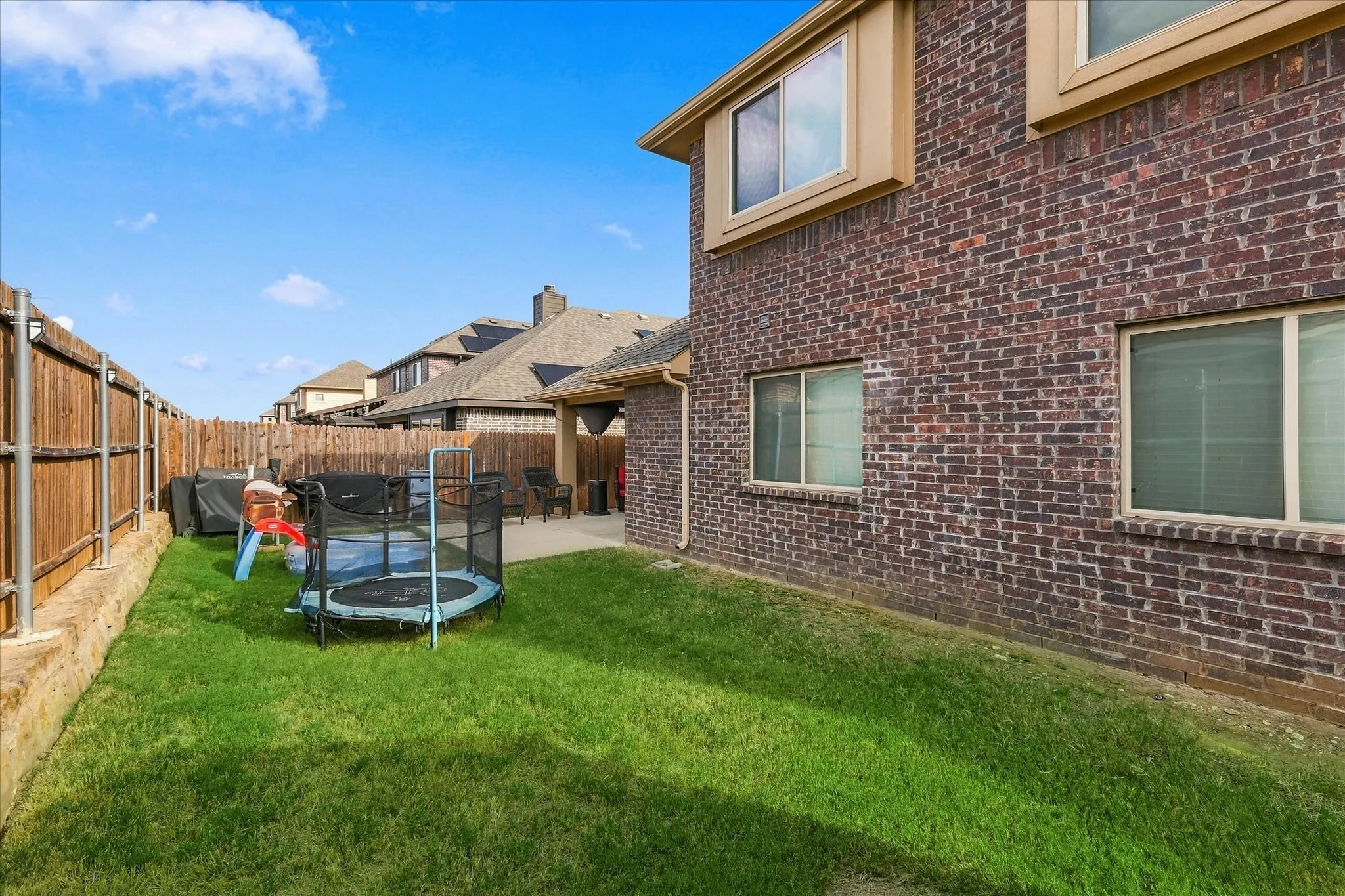 Brick exterior with multiple windows, a covered patio, and a fenced backyard featuring a grassy area