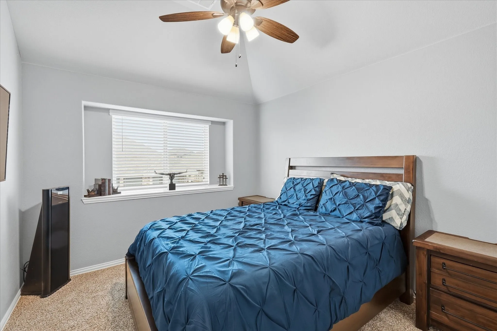 Carpeted bedroom featuring a vaulted ceiling with a ceiling fan, a window with blinds, and light gray wall paint