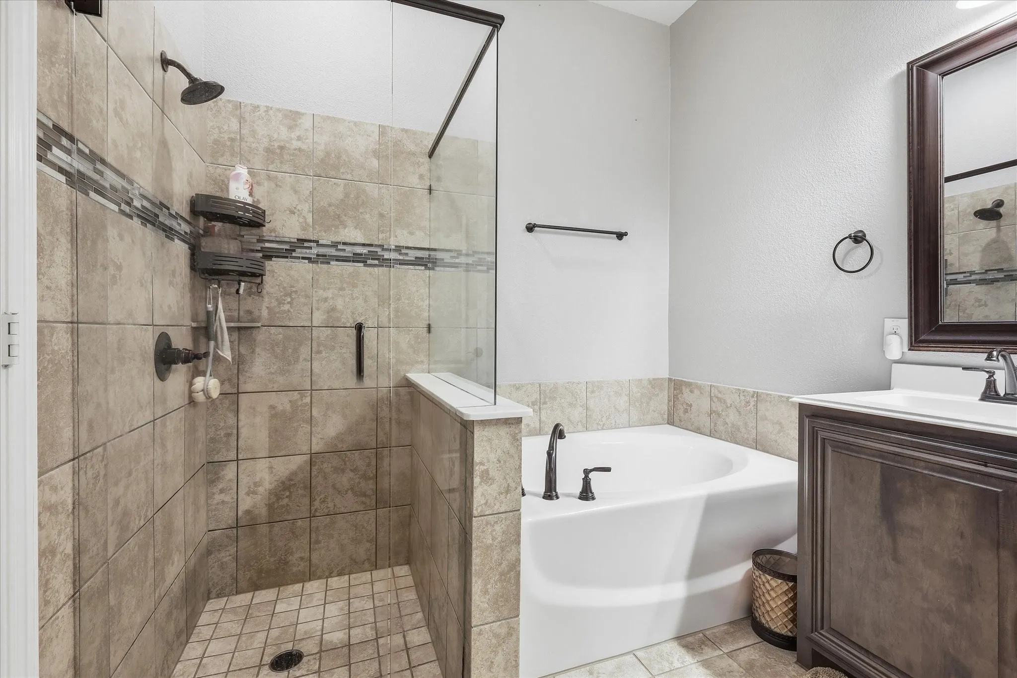 Tiled shower stall with a glass enclosure, a built-in tub, and a dark wood-finish vanity with an integrated sink