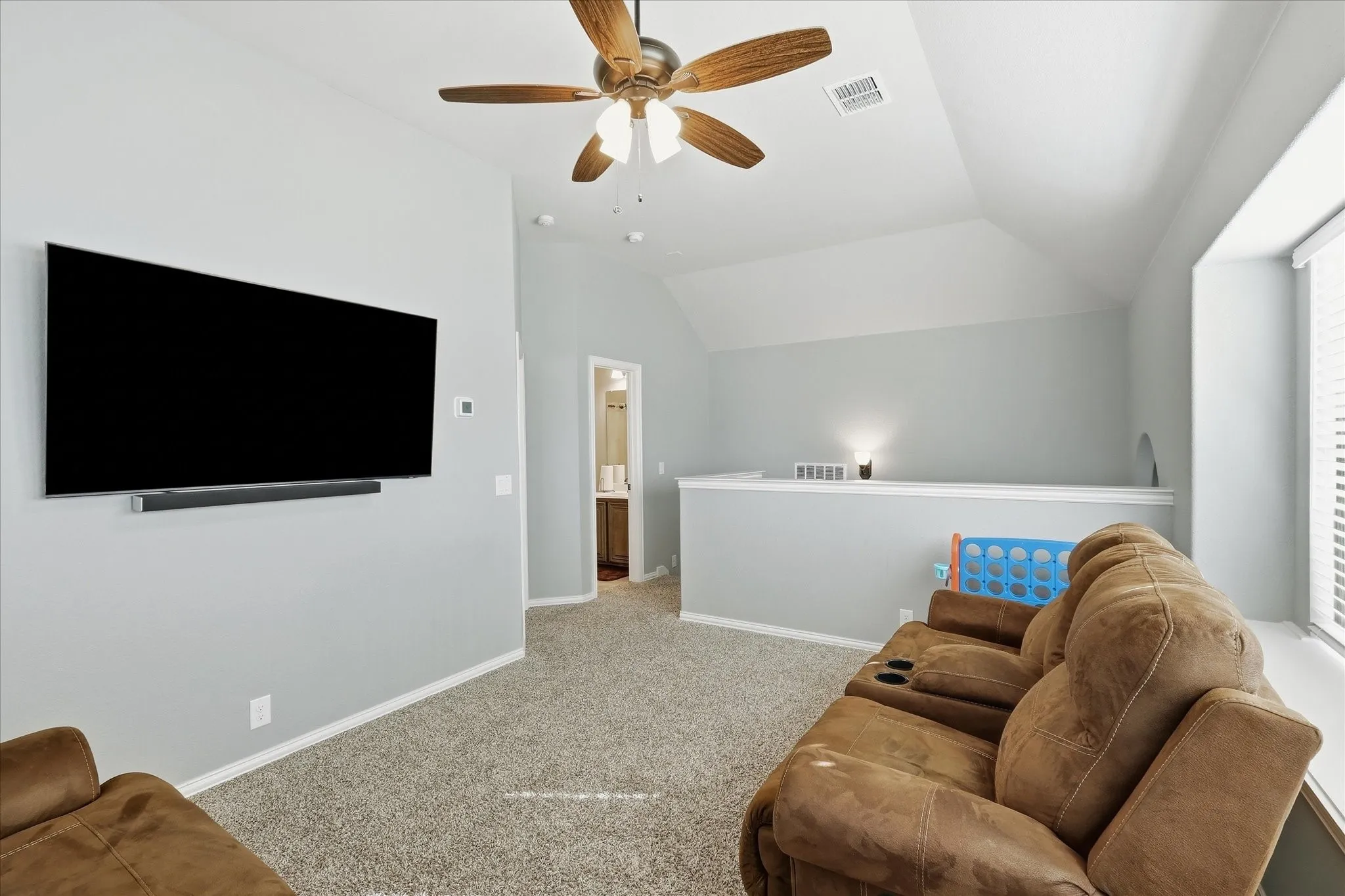 Carpeted bonus room featuring a ceiling fan with integrated lighting, vaulted ceilings, and a half-wall partition
