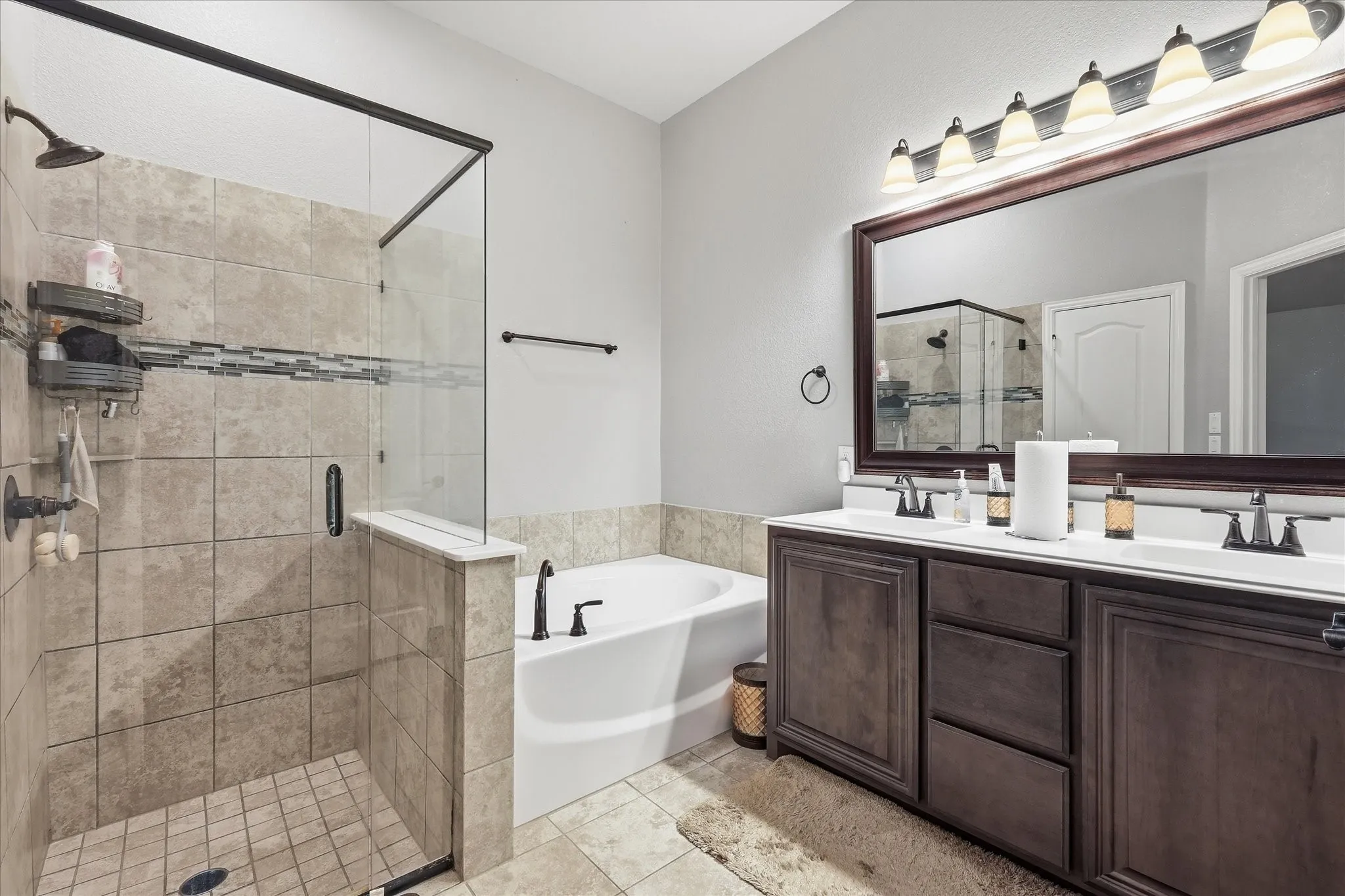 Walk-in shower with tiled surround and glass enclosure, separate soaking tub, and dual vanity with dark wood-finish cabinetry