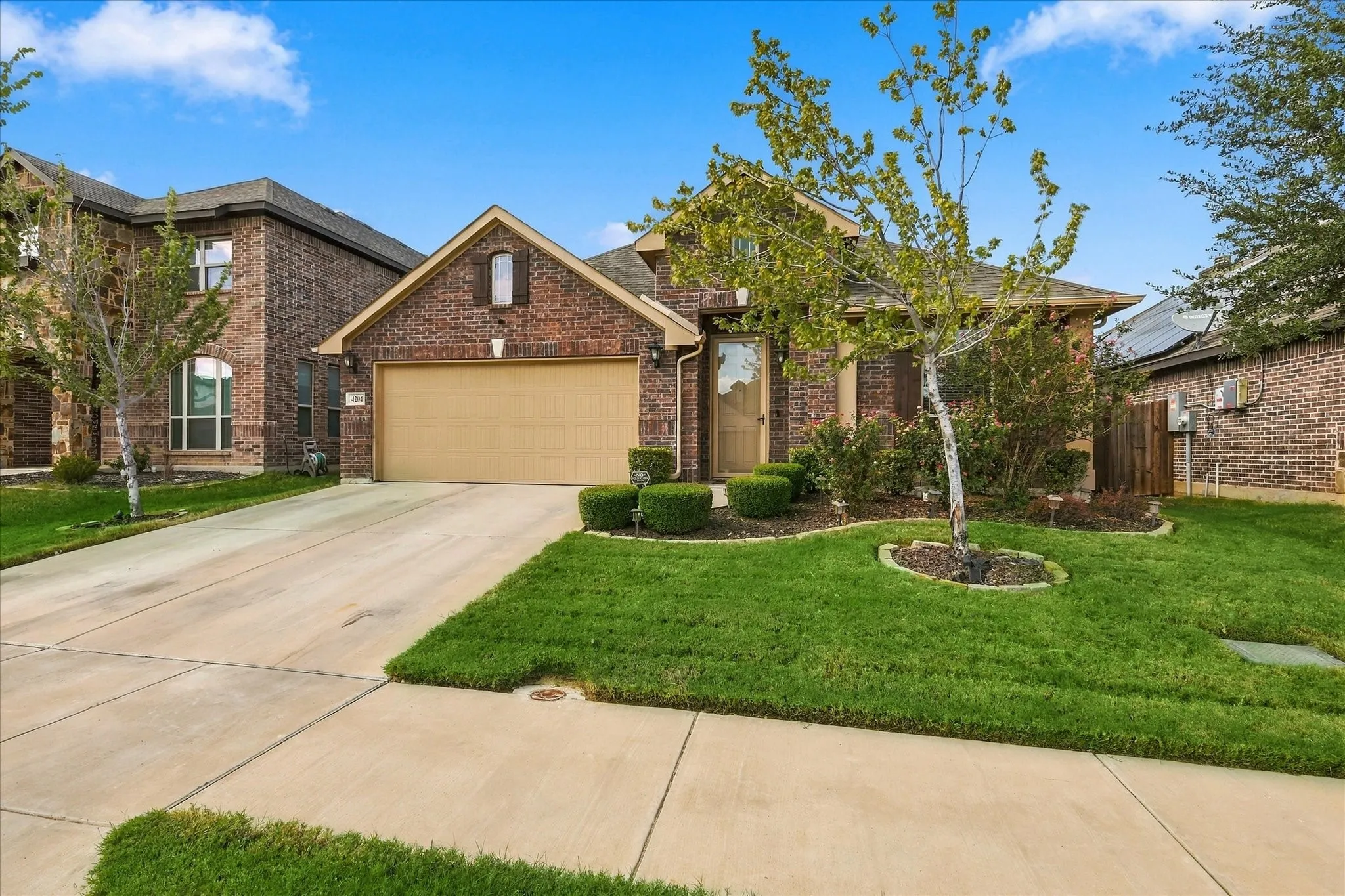 Brick exterior with an attached garage, concrete driveway, and landscaped front yard with mature plantings
