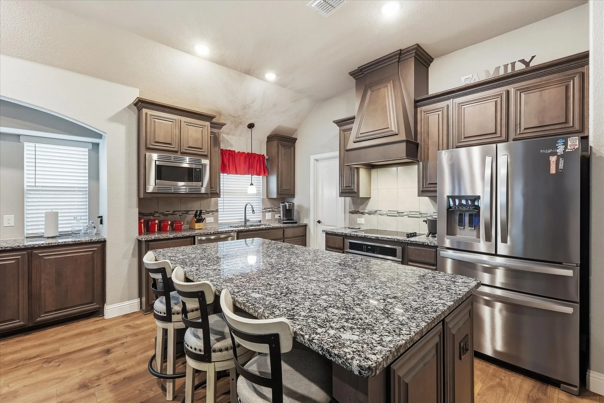 Kitchen featuring a large island with stone countertops, wood-finish flooring, dark wood cabinetry, and stainless steel appliances