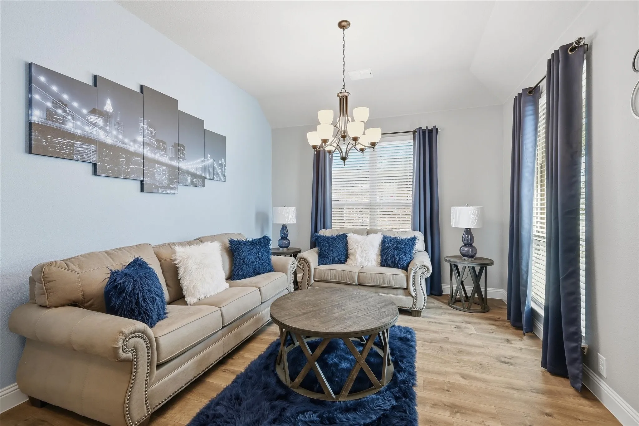 Recessed ceiling with an ornate chandelier, wood-finish flooring, and multiple windows with blinds