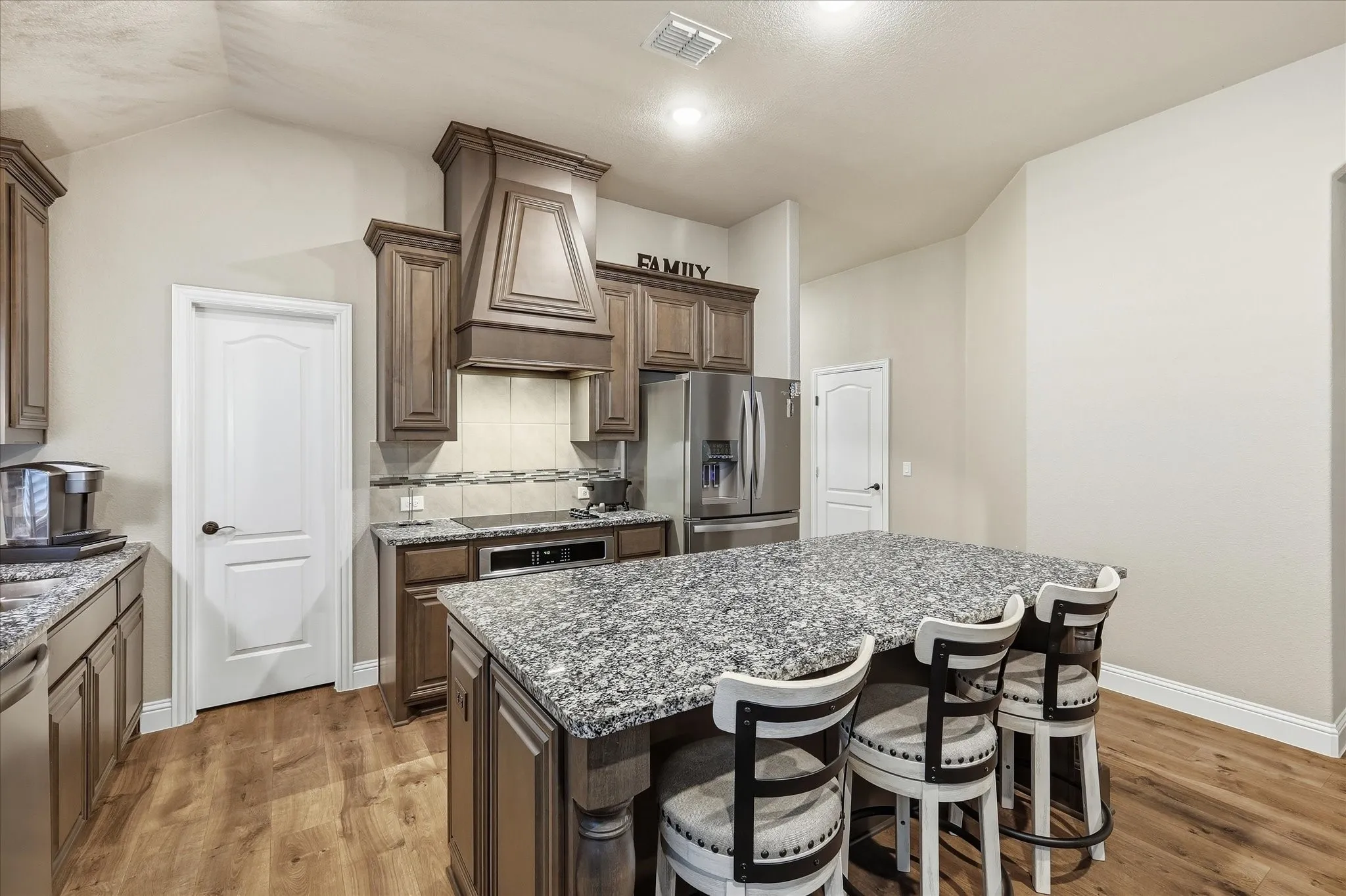 Kitchen featuring wood-finish flooring, stained wood cabinetry, stainless steel appliances, a large central island with seating, and granite countertops