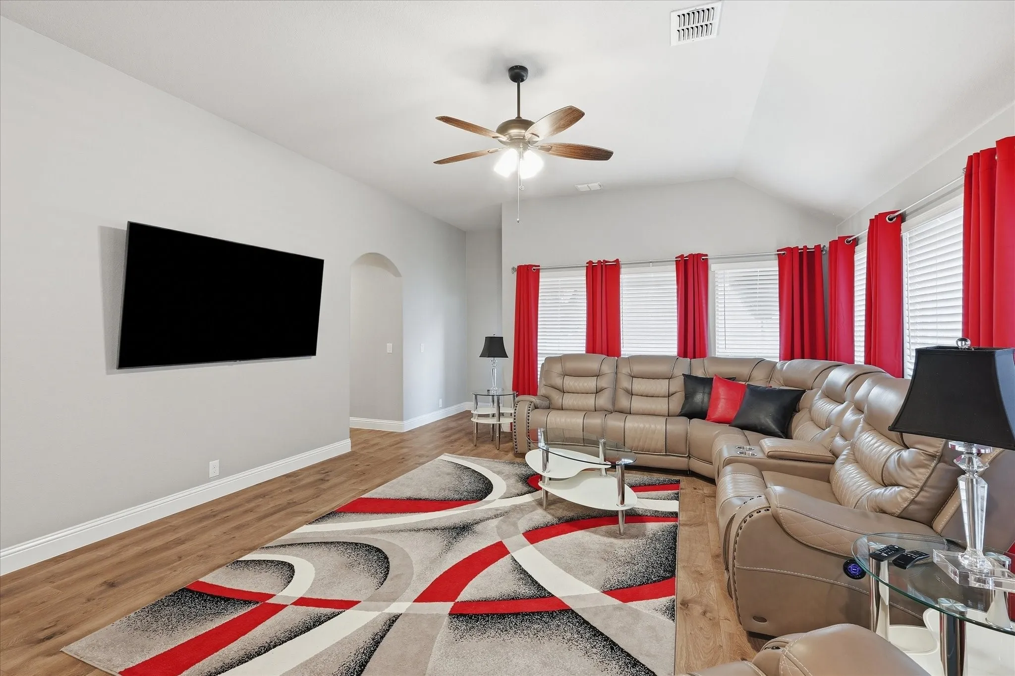 Vaulted ceiling, wood-finish flooring, ceiling fan with integrated lighting, wall-mounted display, and an arched doorway