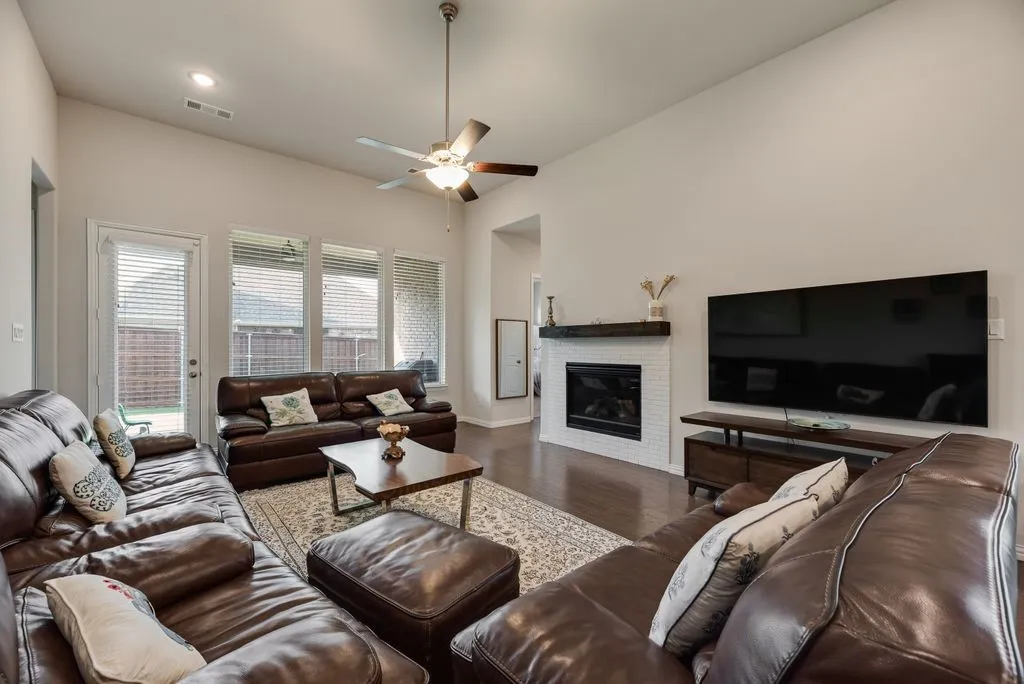 Living area featuring vaulted ceilings, wood-finish flooring, a contemporary fireplace with white tile surround and wood mantel, recessed lighting, and a ceiling fan
