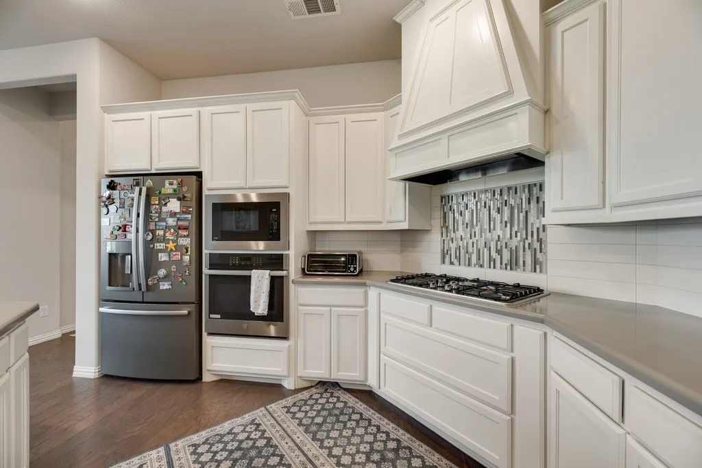 Contemporary kitchen featuring white cabinetry, integrated stainless steel appliances, a gas cooktop, and a decorative tile backsplash under a custom range hood